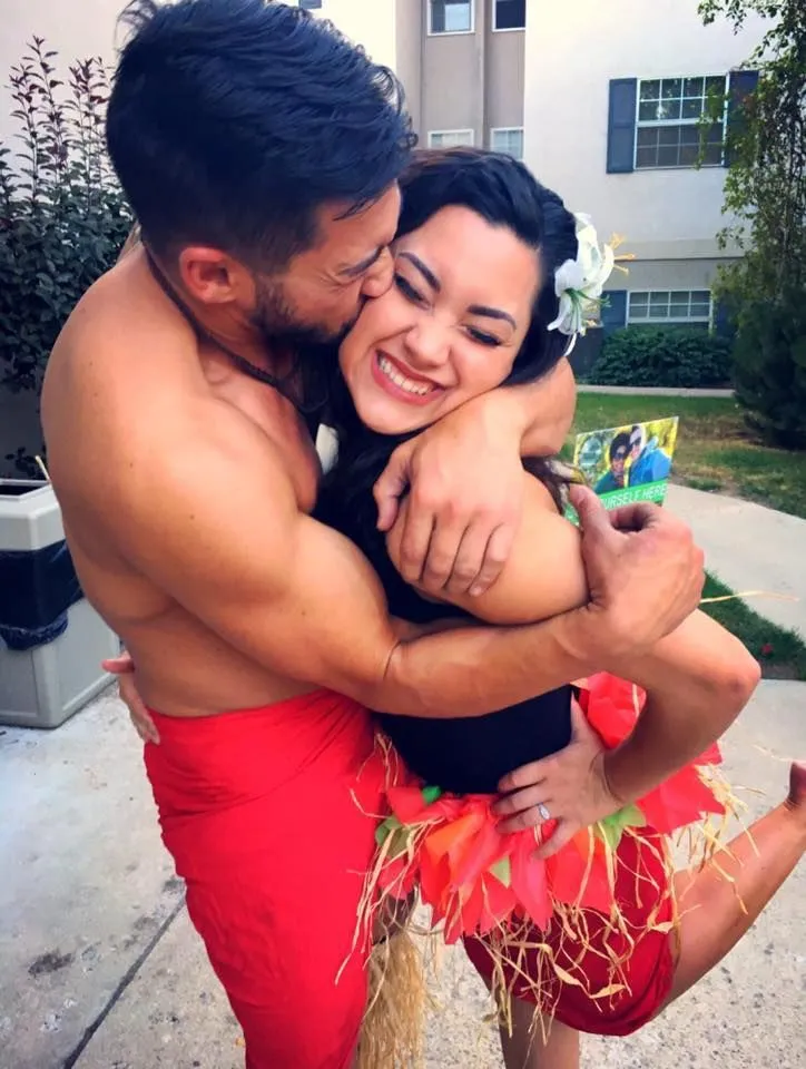A shirtless man is holding a woman in his arms and kissing her on the cheek