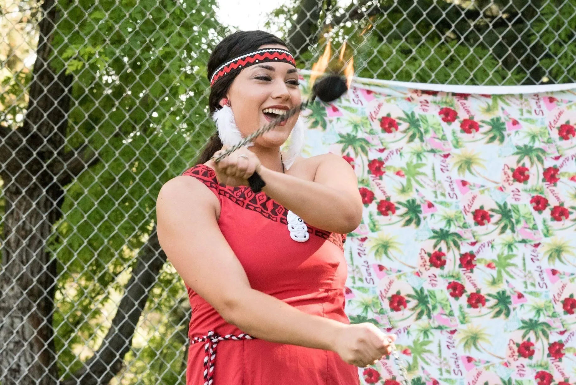 A woman in a red dress is holding a torch in front of a chain link fence.