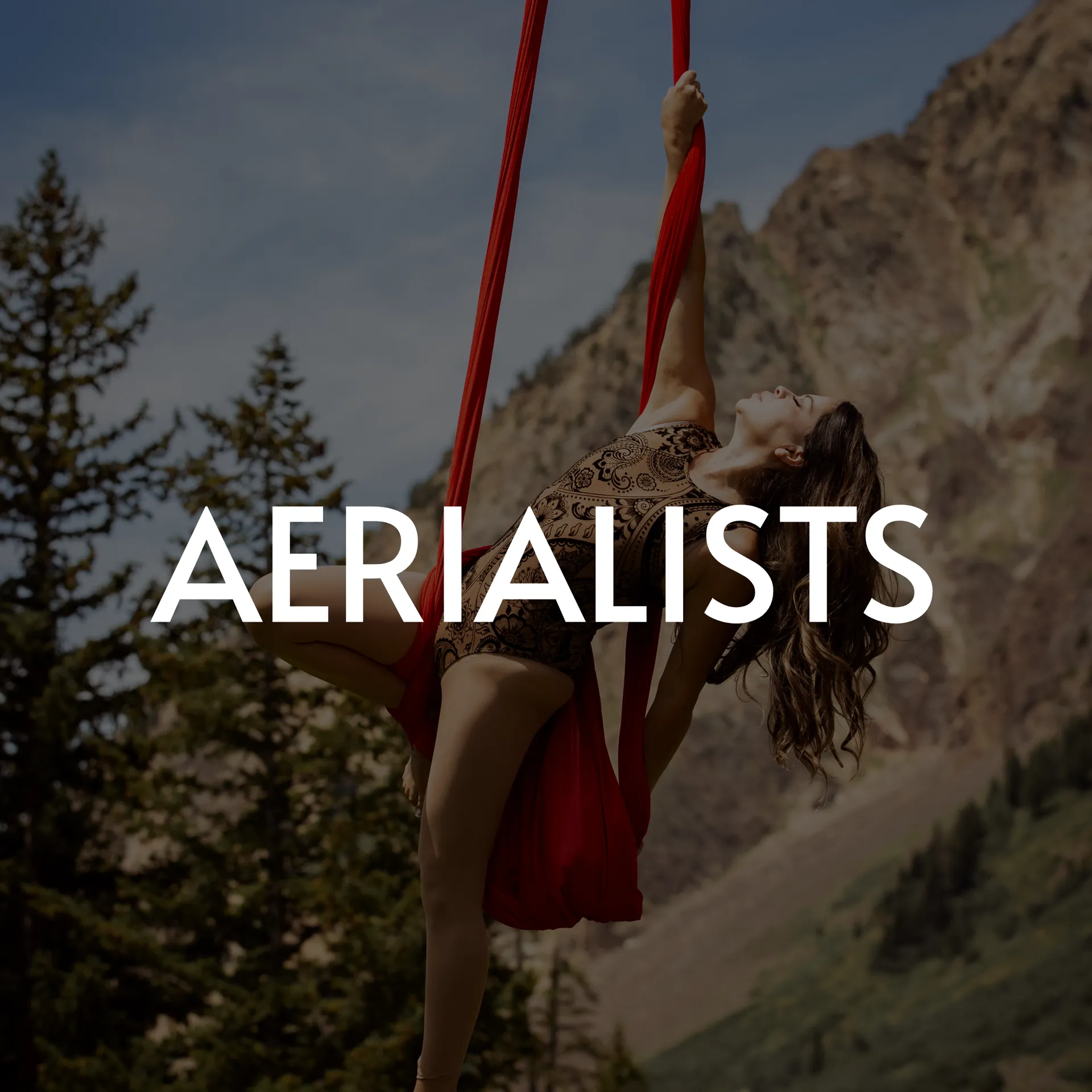 Woman performing aerial silk routine outdoors, red fabric, mountains.