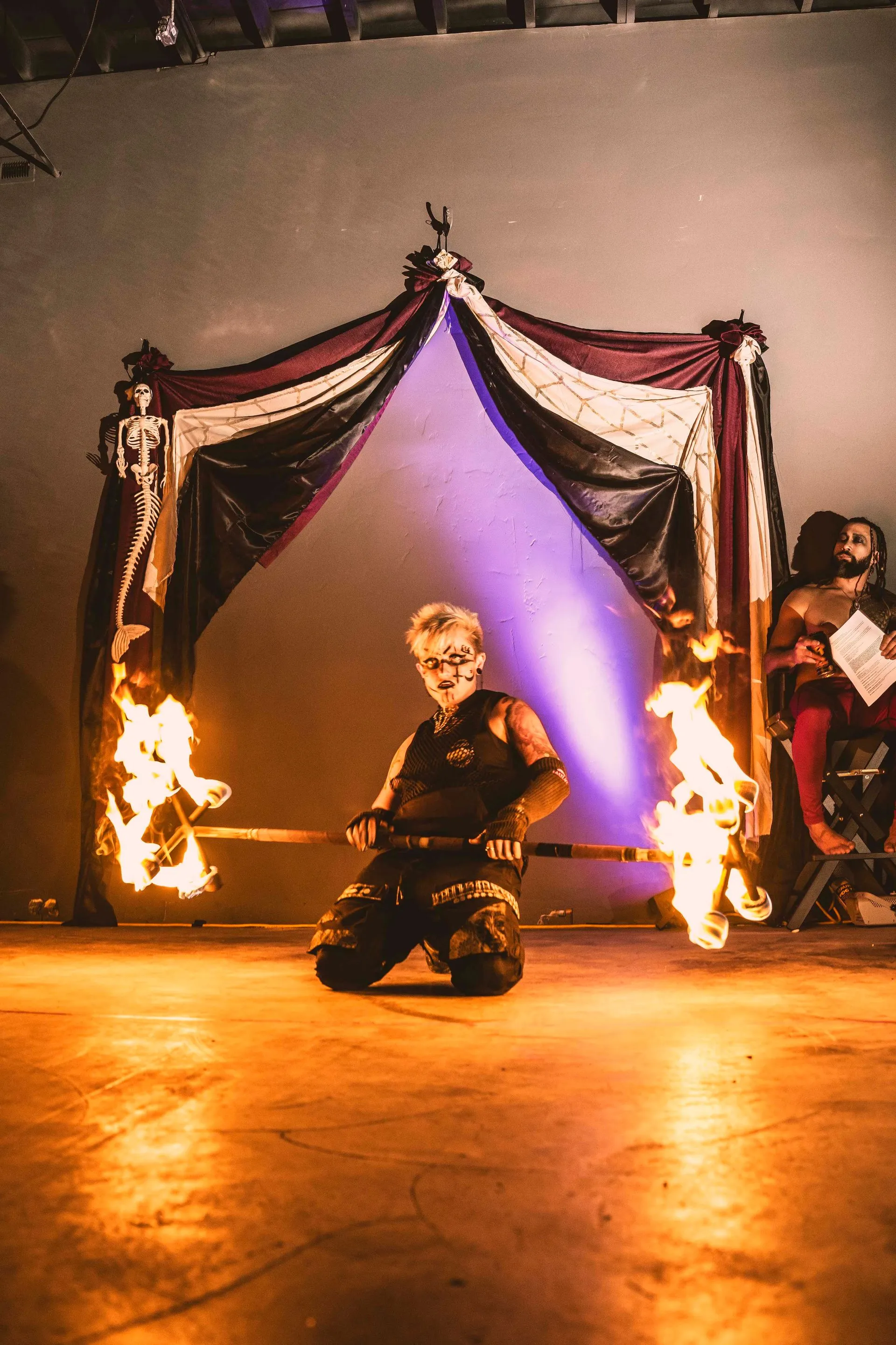 A man is kneeling down in front of a curtain with flames coming out of it.