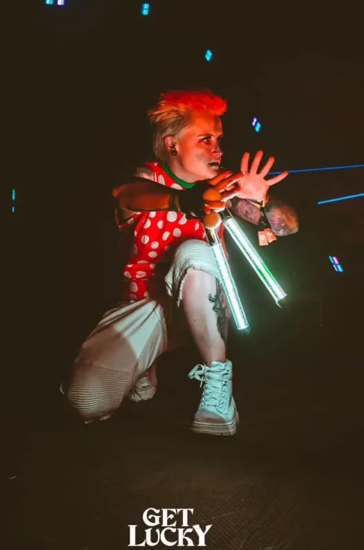 A woman in a red and white polka dot shirt is kneeling down in the dark holding glow sticks.
