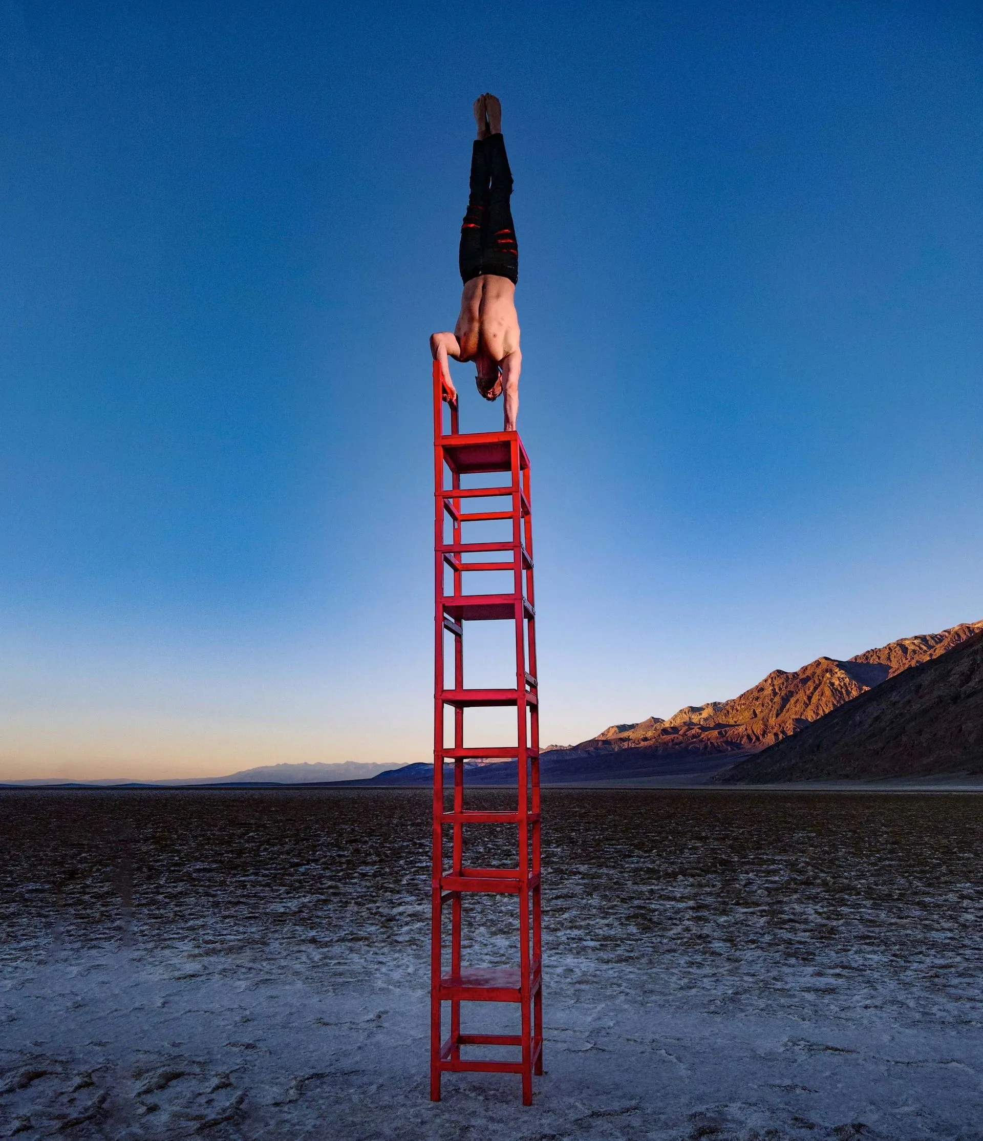 A man is doing a handstand on top of a red ladder
