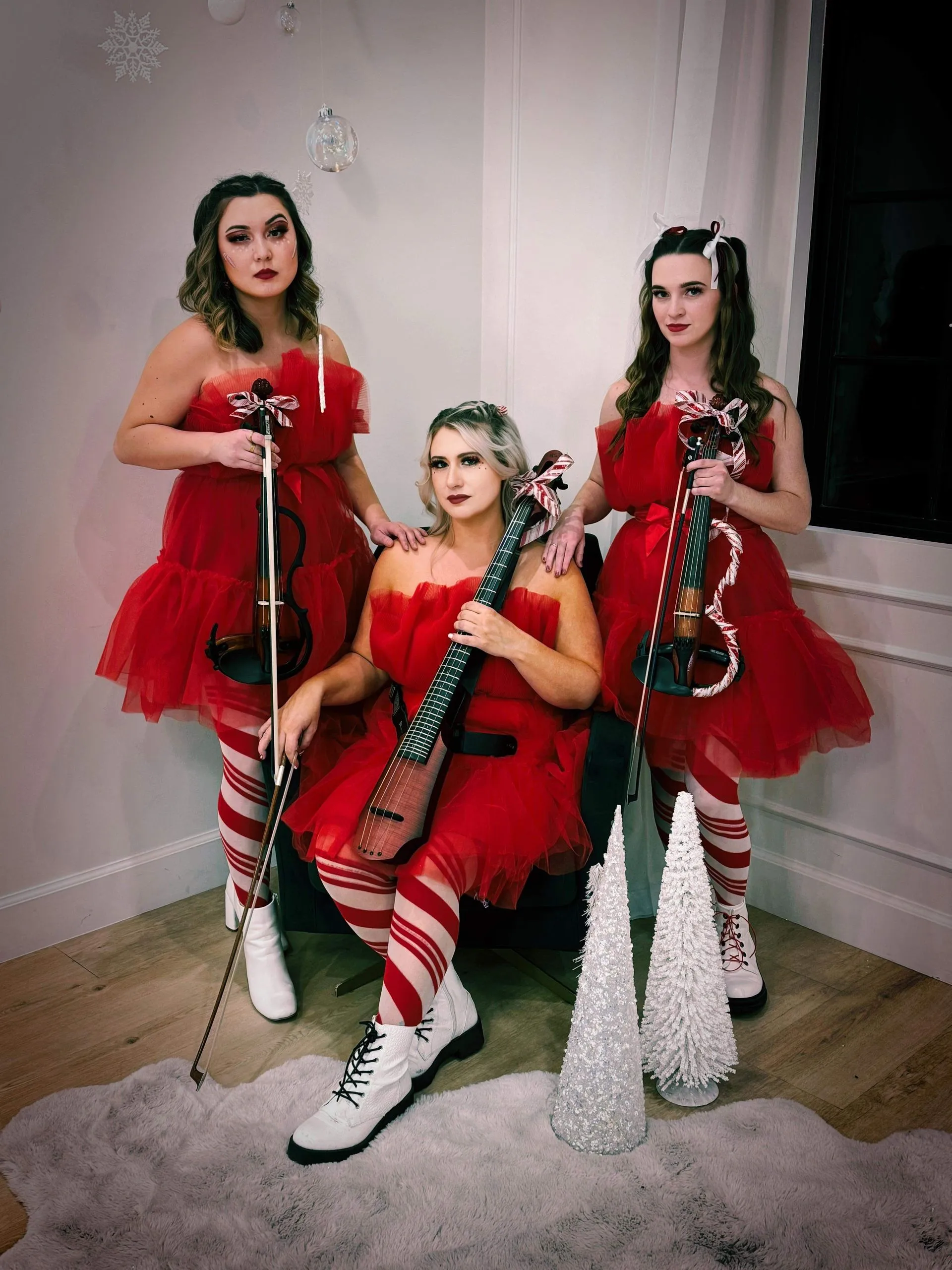 Three women in red dresses are playing violins in a room.