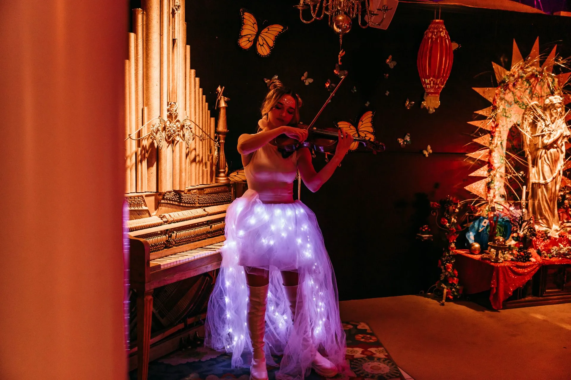 A woman in a light up skirt is playing a violin in a dark room.