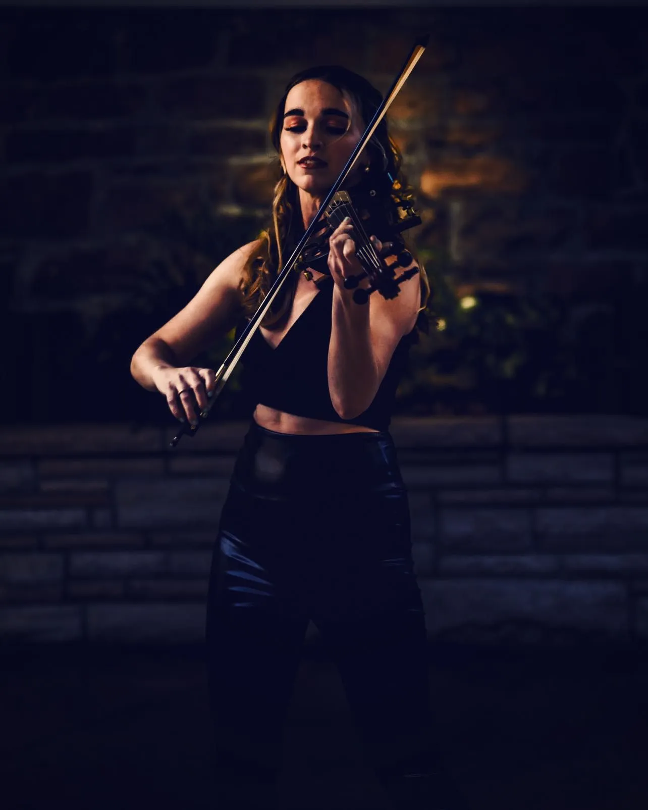 A woman is playing a violin in a dark room.