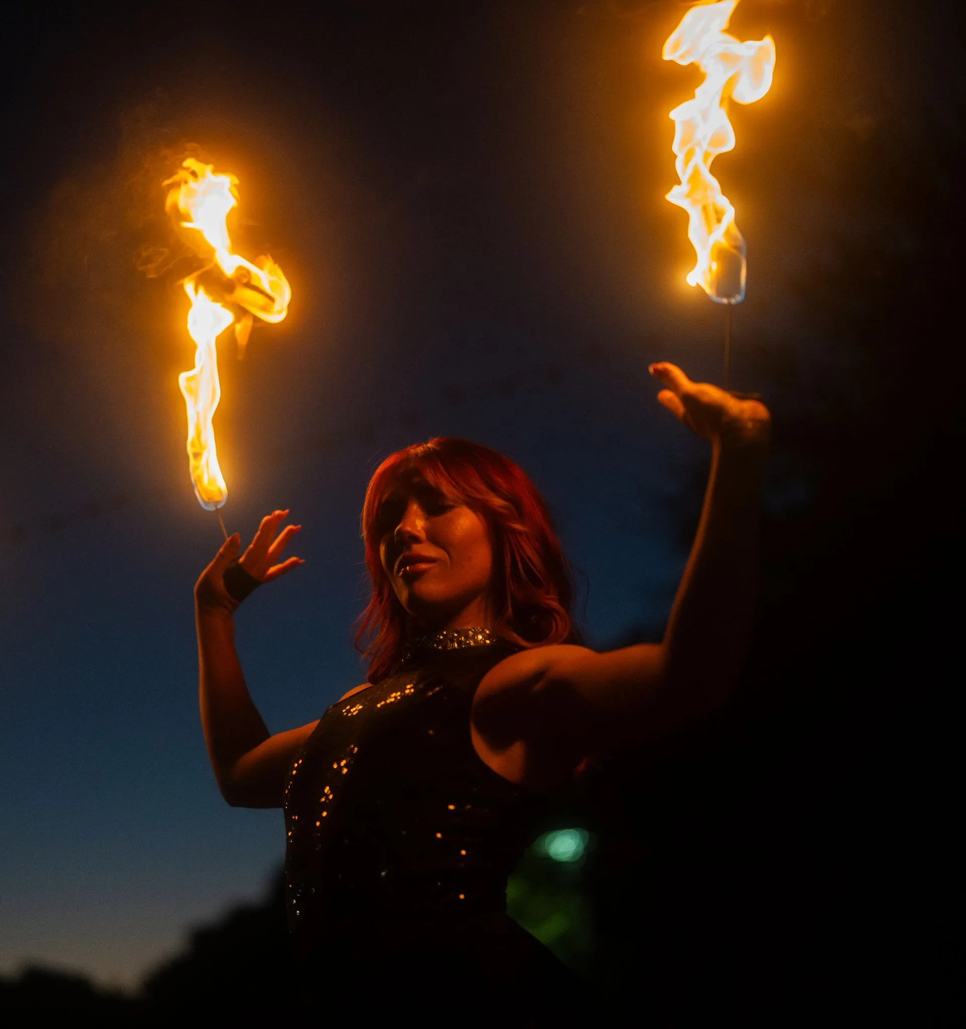 A woman is holding two fire torches in her hands at night.