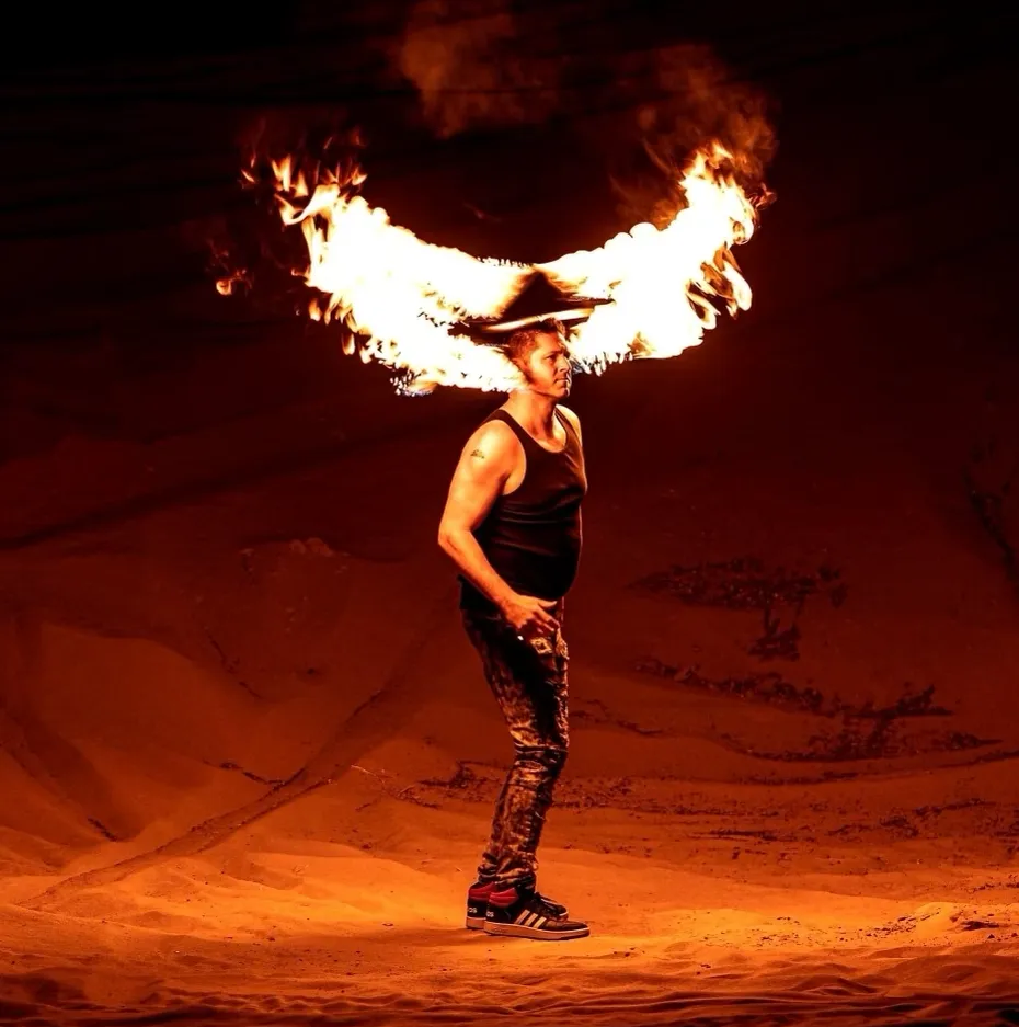 A man wearing a cowboy hat is blowing flames out of his mouth