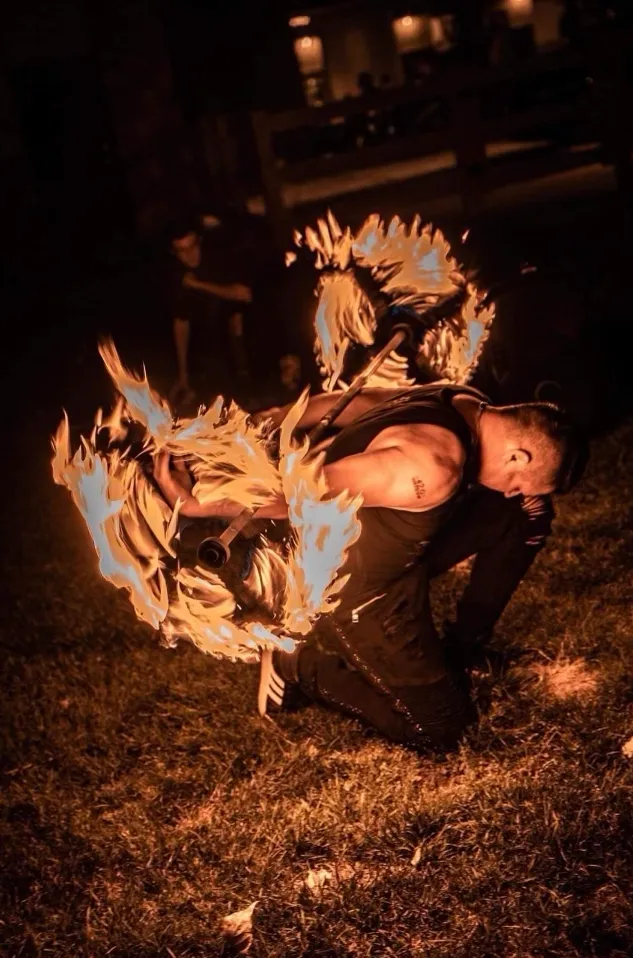 A man is kneeling down in the grass with a fireball in his hand.