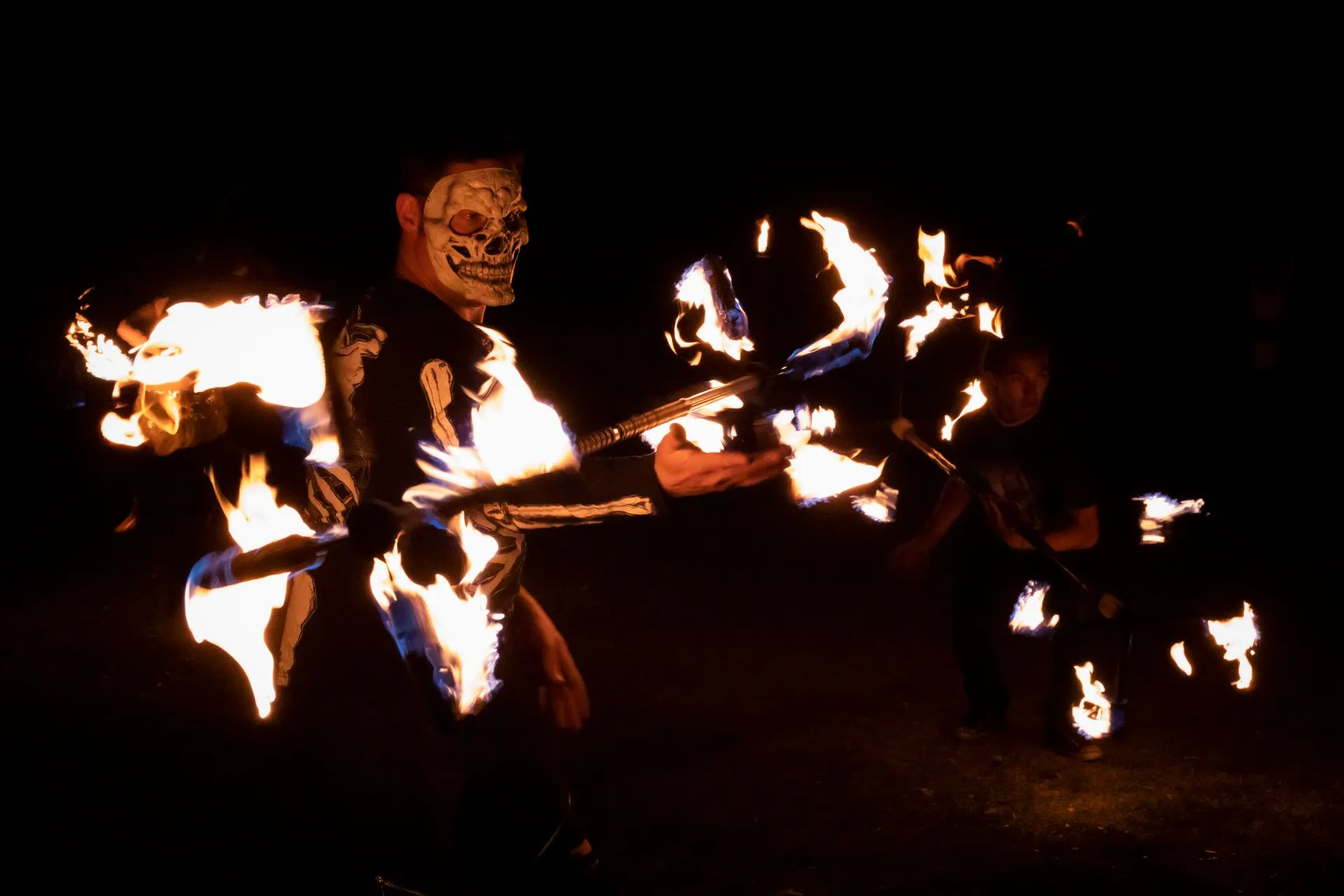 A man in a skeleton costume is holding a fire stick in the dark.