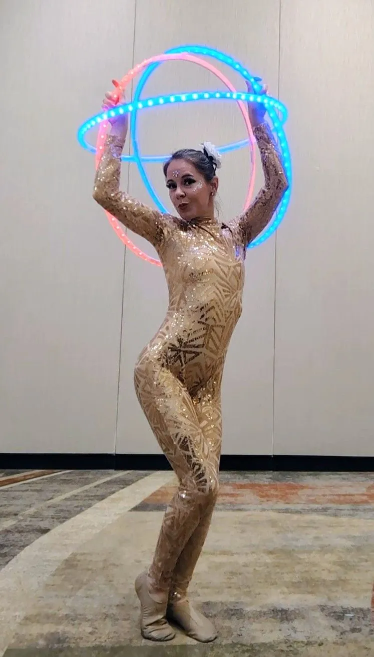 A woman in a gold bodysuit is holding a hula hoop in her hands.