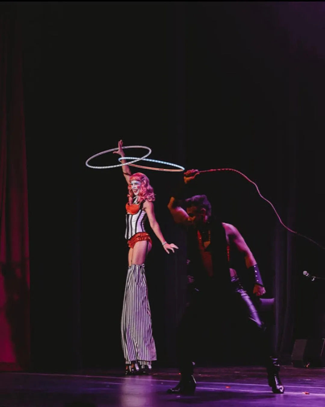 A man and a woman are performing hula hoops on stilts on a stage.