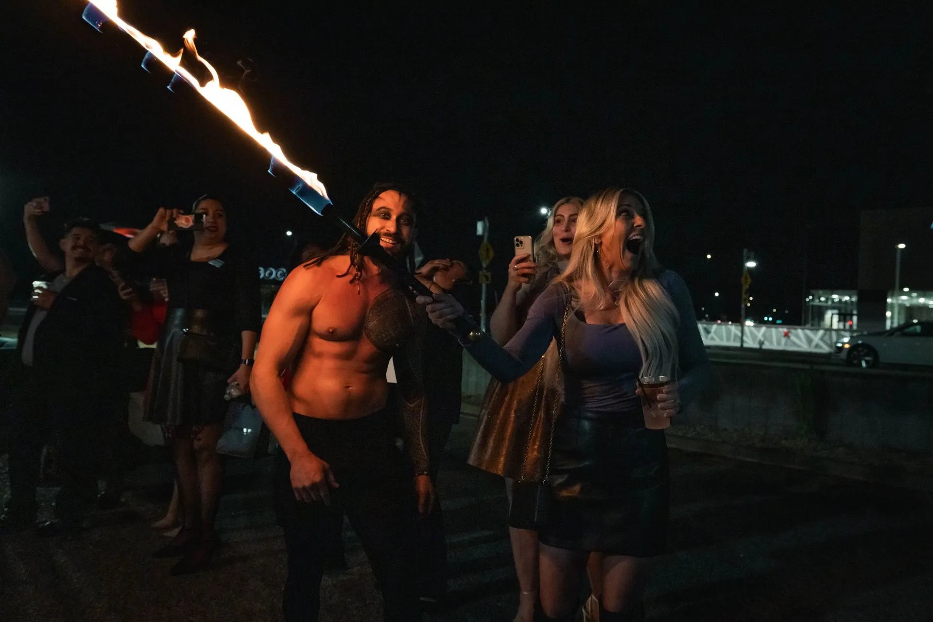 A group of people are standing around a shirtless man holding a torch.
