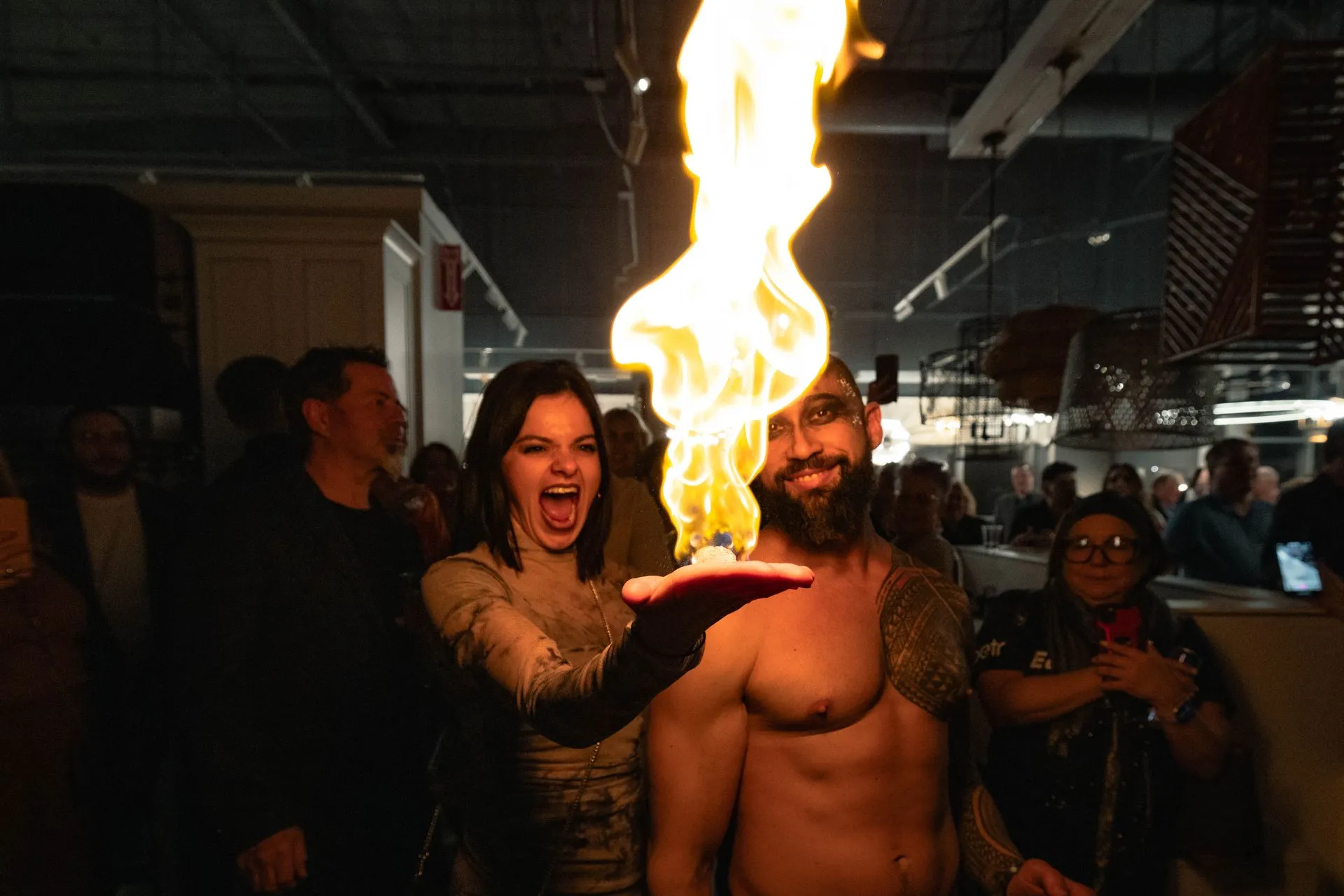 A woman is holding a fireball in front of a shirtless man.