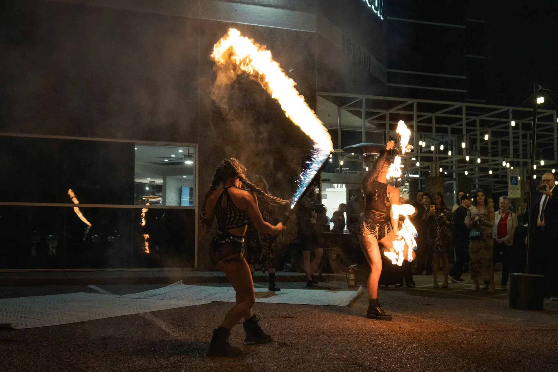 Two women are performing a fire show in front of a crowd at night.