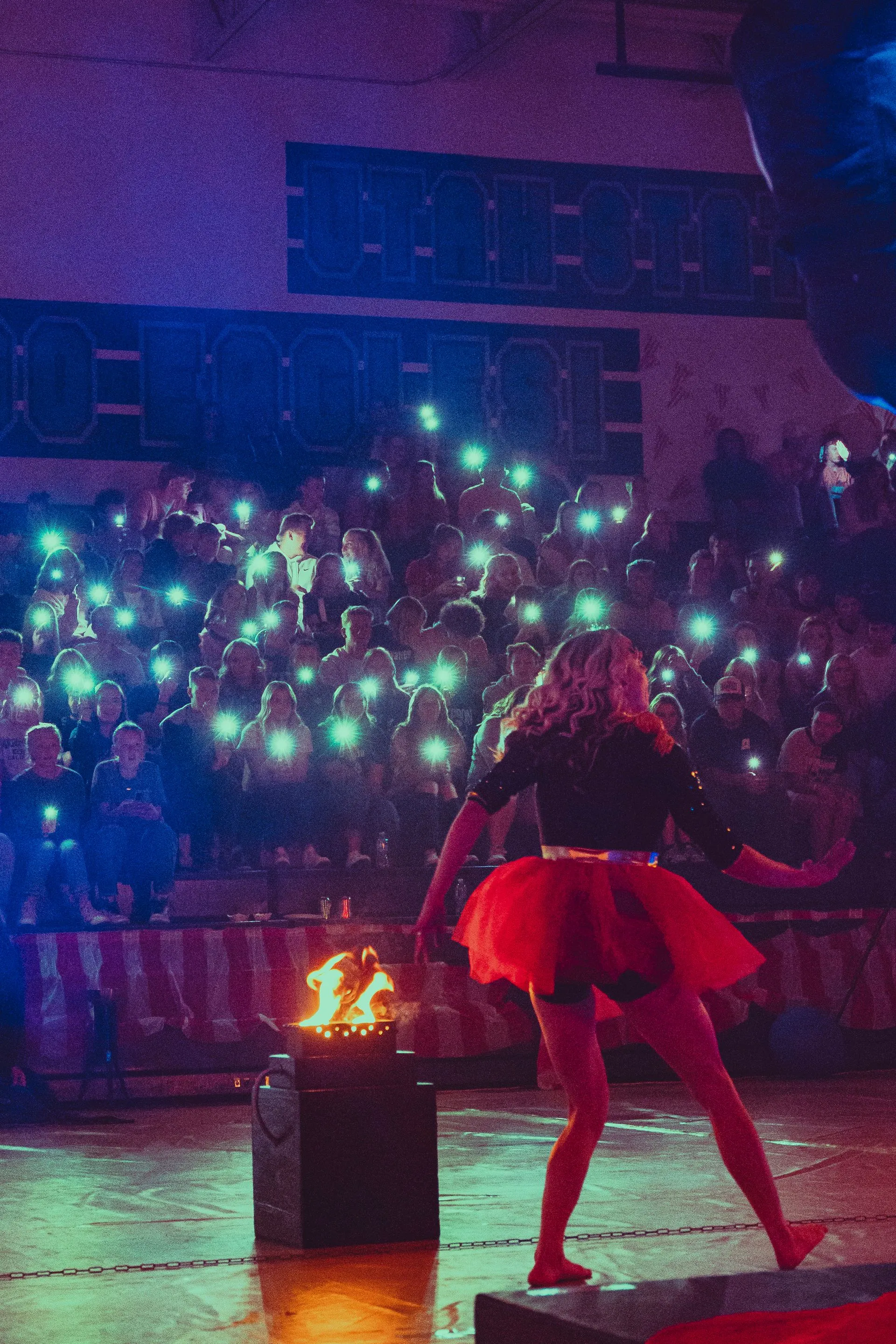 A woman in a red tutu is dancing on a stage in front of a crowd.