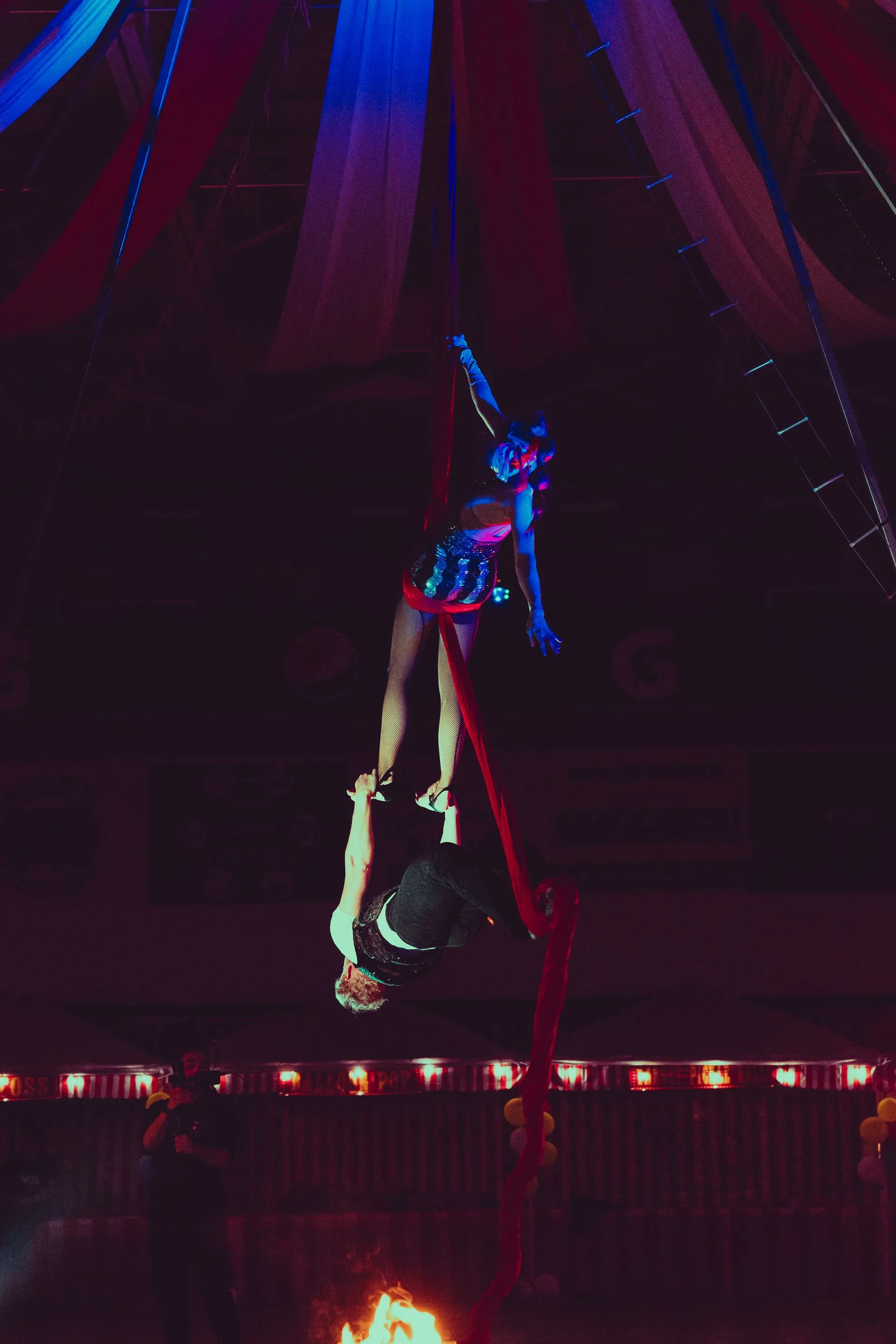 A woman is performing aerial acrobatics in a circus tent.