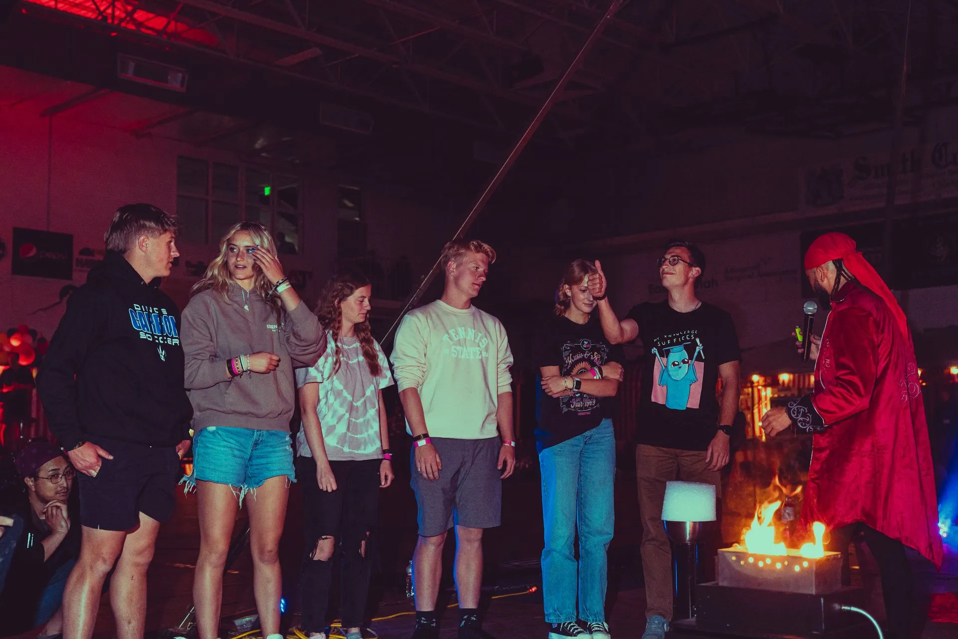 A group of people are standing in front of a fire in a dark room.