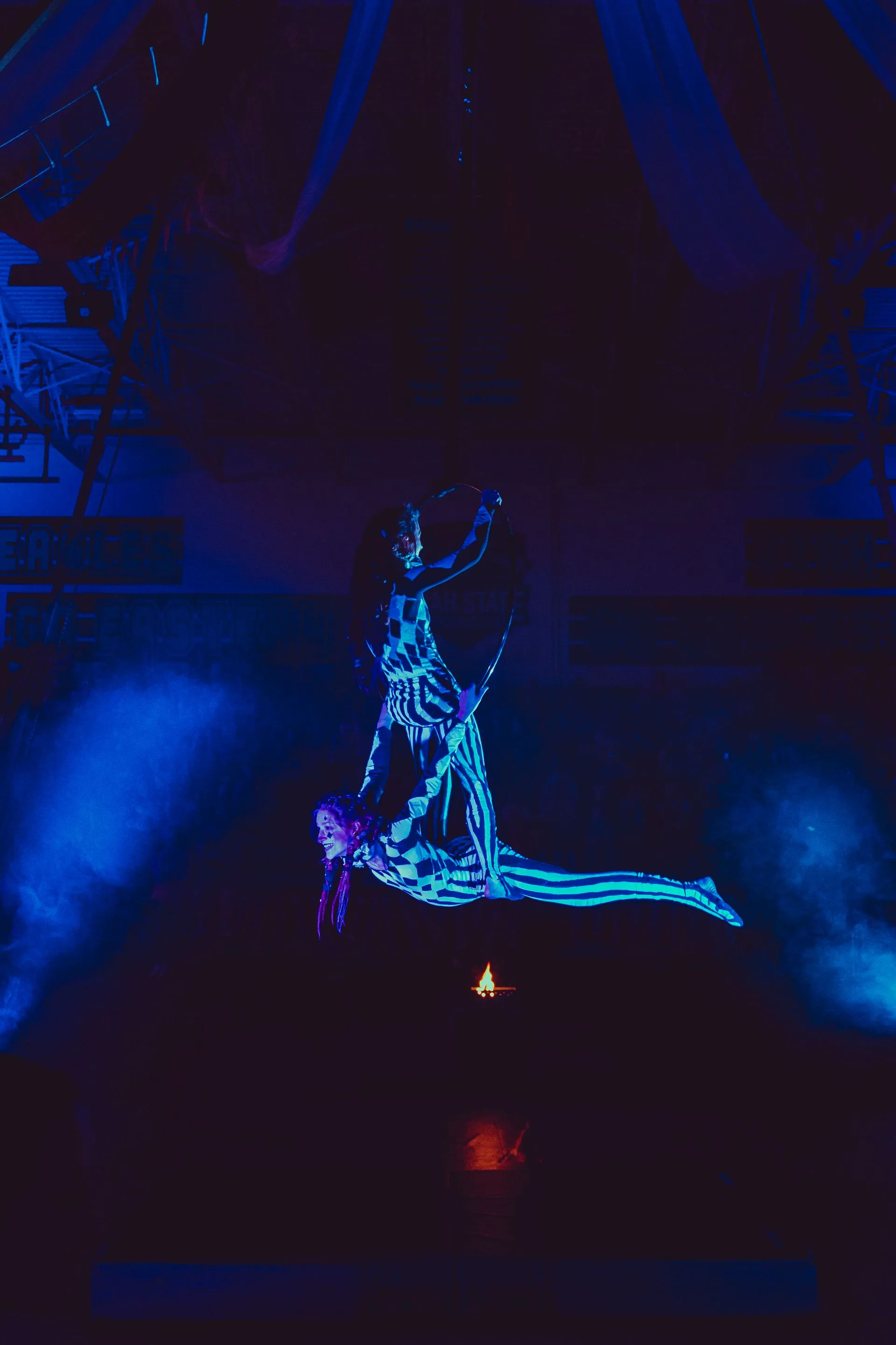 A man and a woman are performing aerial acrobatics in a dark room.