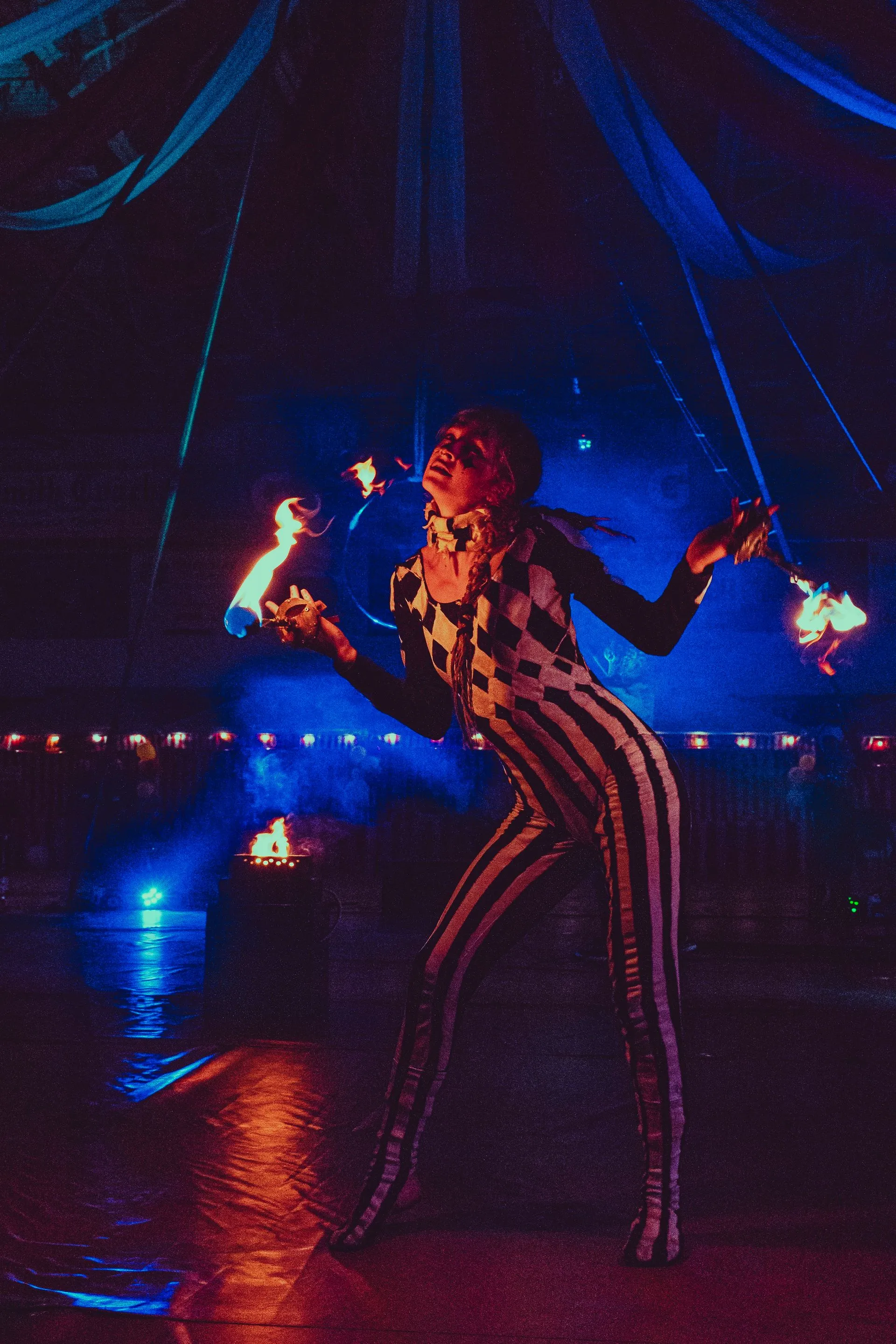 A woman in a striped jumpsuit is juggling fire in a dark room.