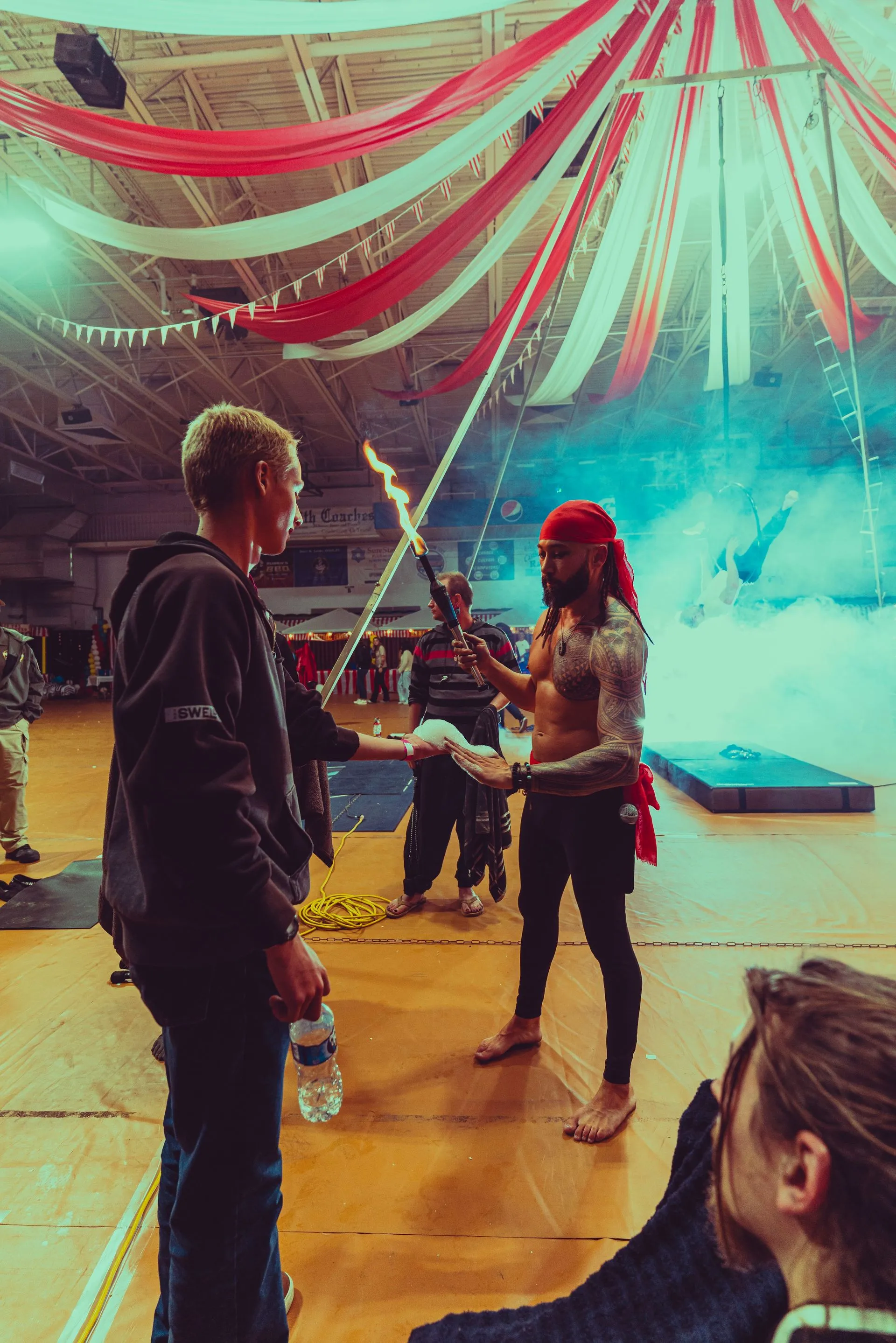 A man in a pirate costume is holding a fire stick in a gym.