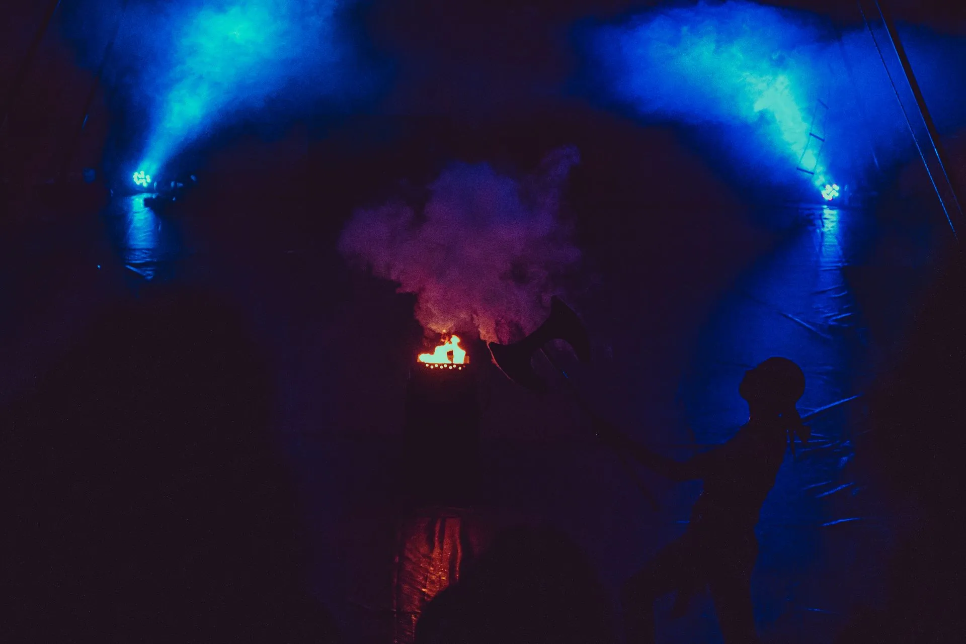 A person is standing in front of a stage with blue lights and smoke coming out of it.