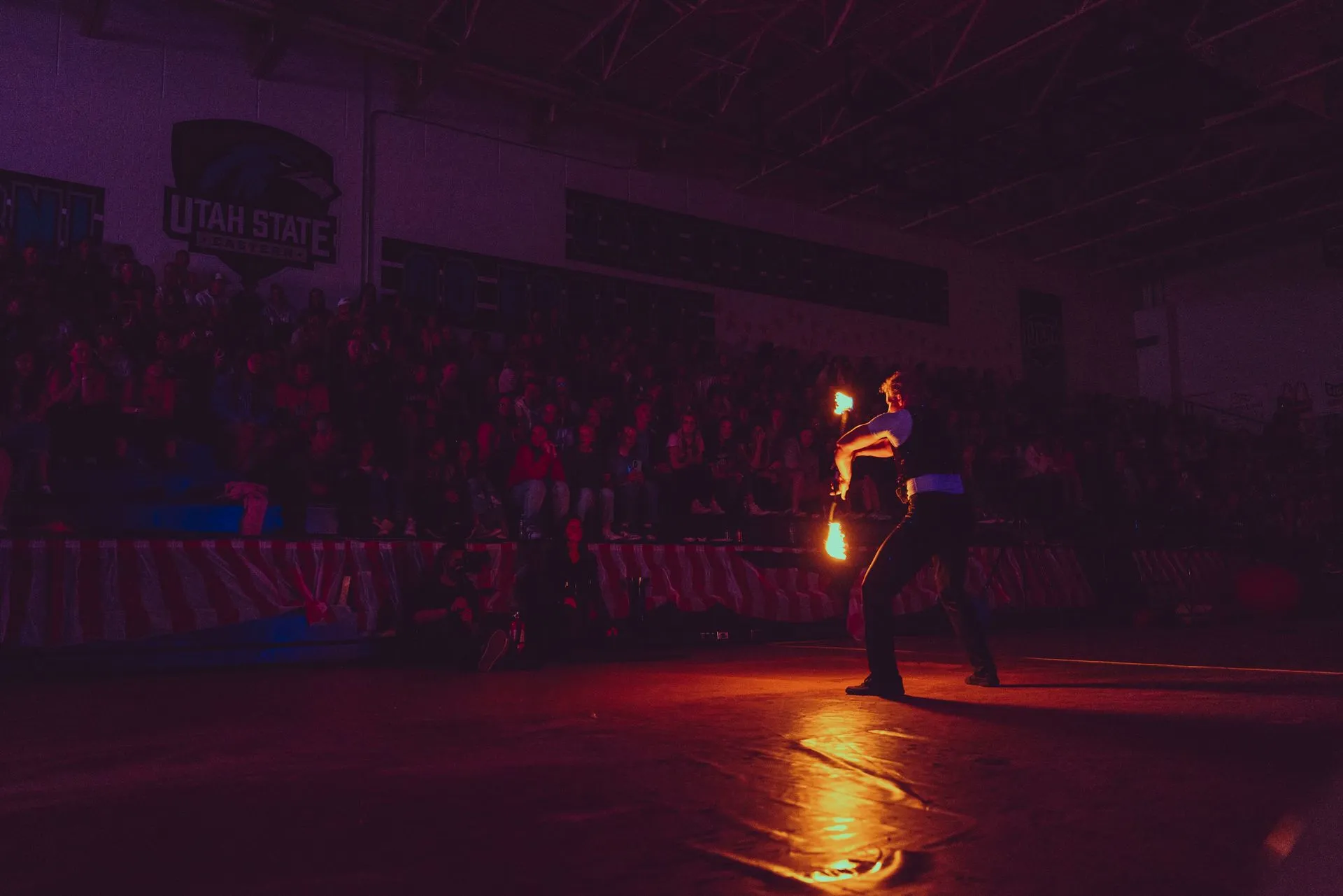 A man is holding a fireball in a dark room in front of a crowd.
