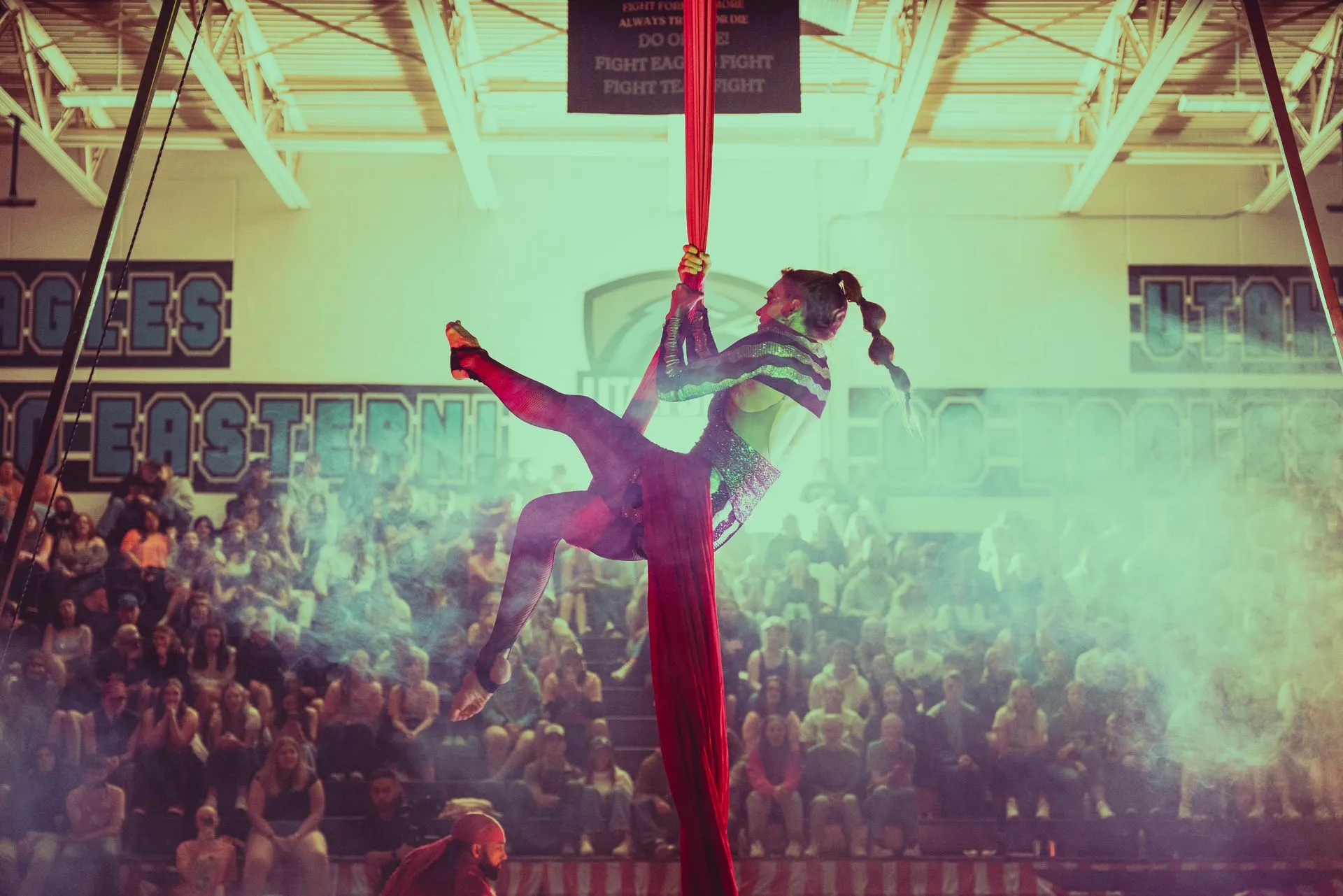 A woman is performing aerial acrobatics in front of a crowd in a gym.