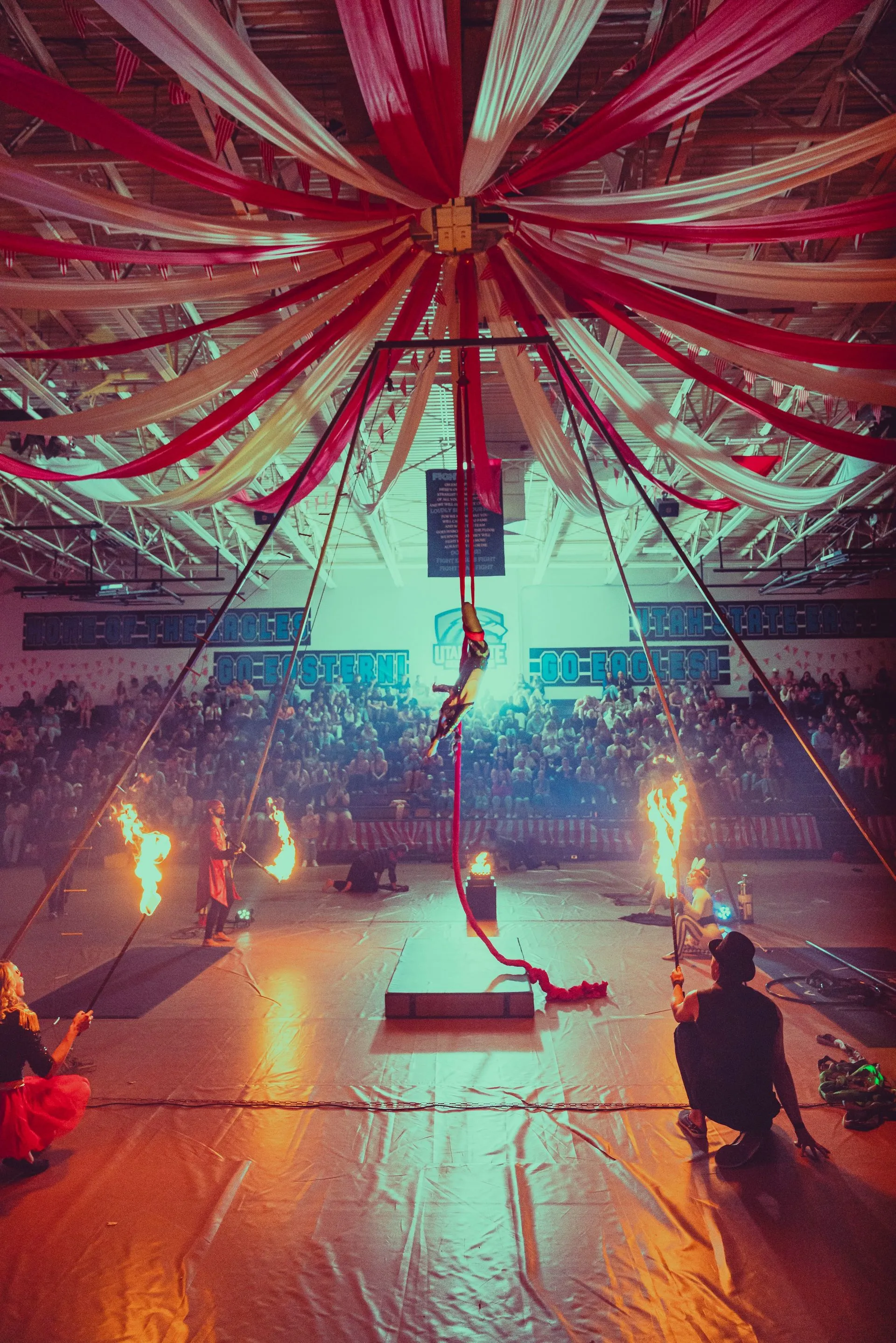 A man is sitting on the floor in a gym watching a circus performance.