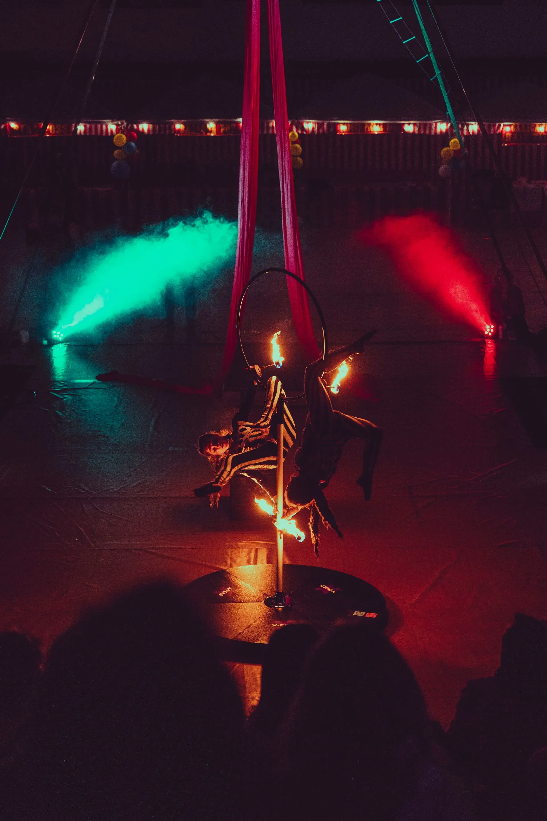A person is performing aerial acrobatics on a pole in a dark room.