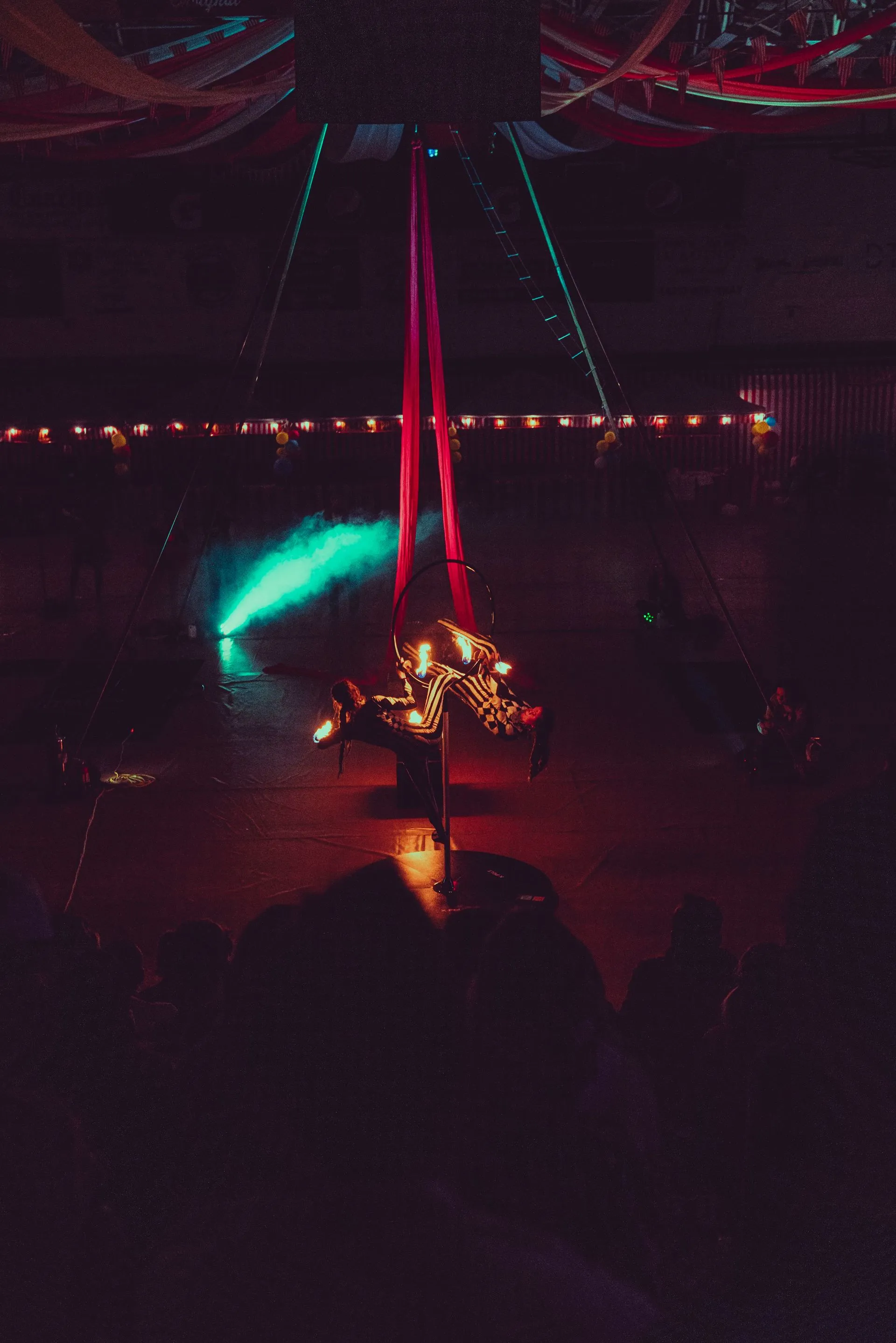 A person is hanging from a red aerial silk in a dark room.