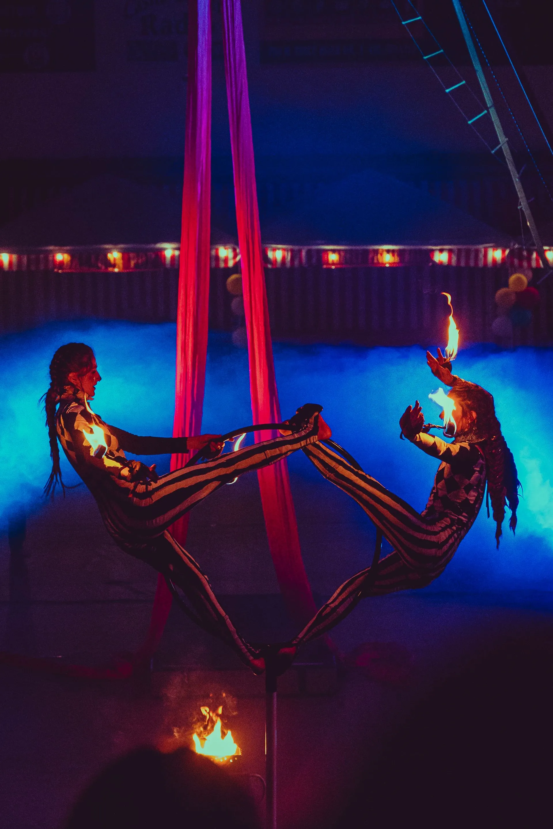 Two aerial acrobats are performing aerial tricks in a dark room.