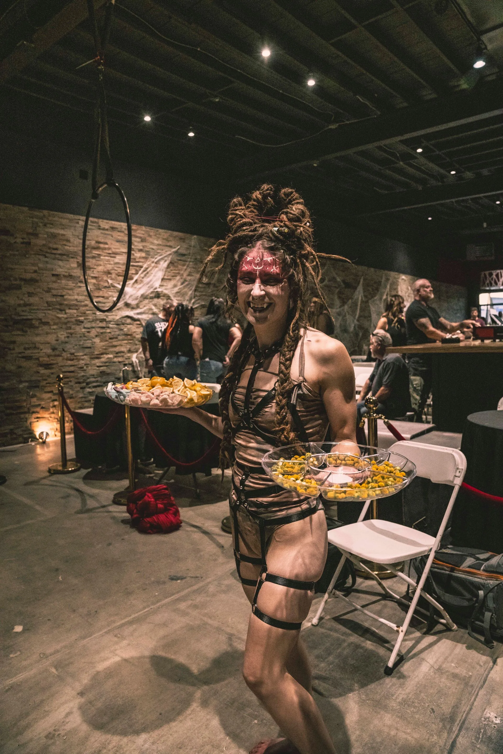 A woman in a medusa costume is holding a tray of food in a room.