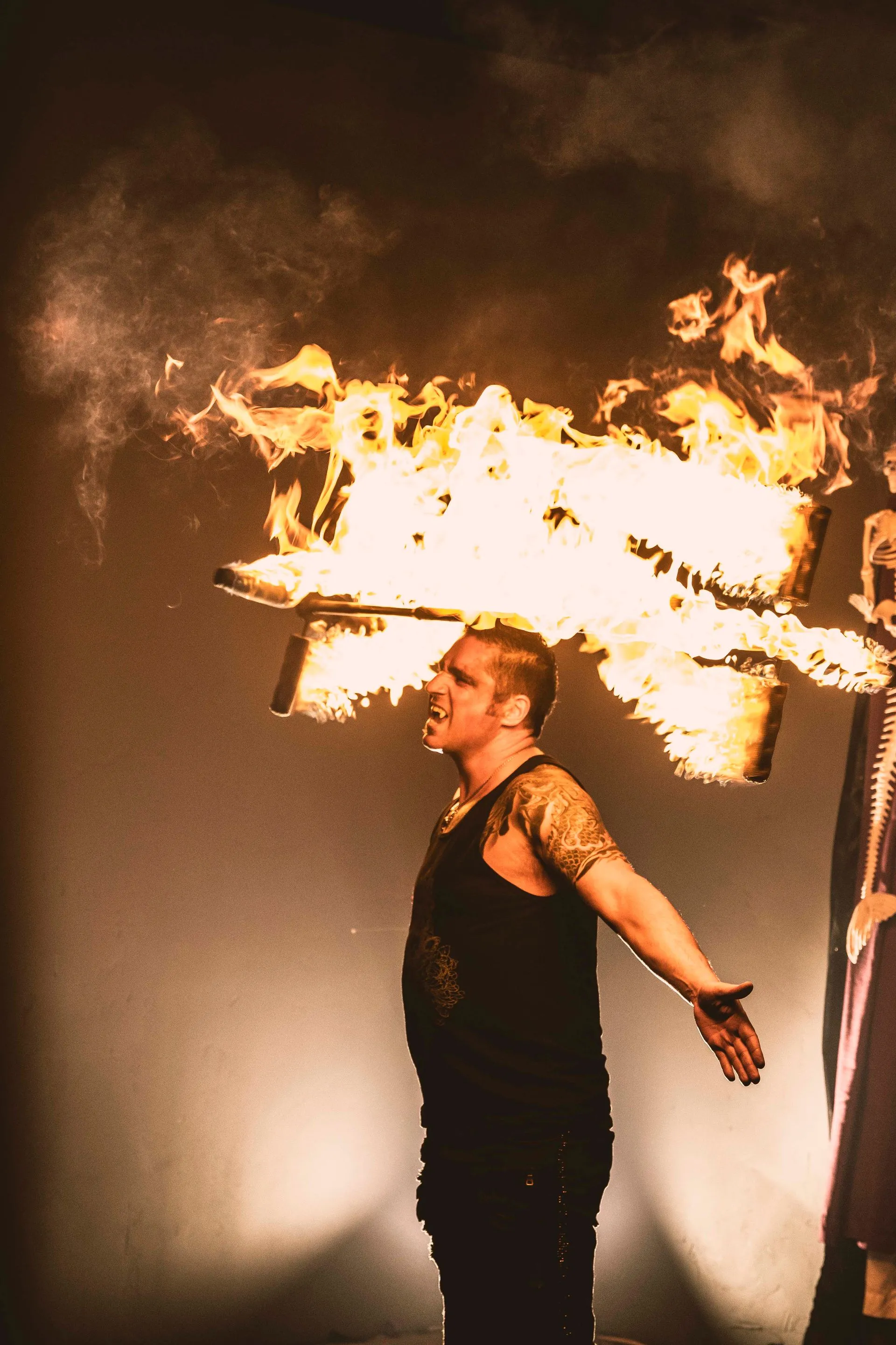A man with a tattoo on his arm is blowing flames out of his mouth.