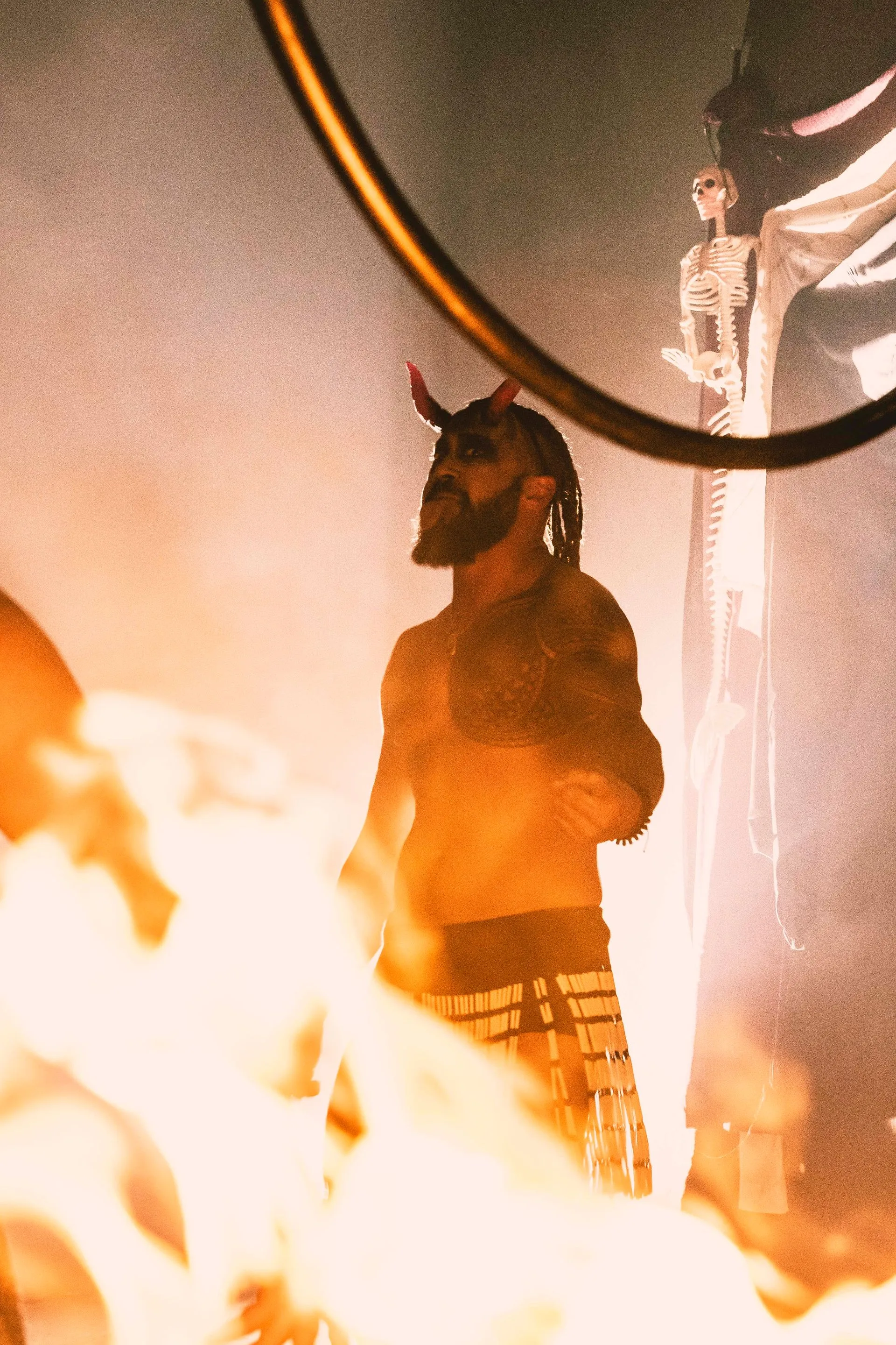 A man with horns is standing in front of a fire.