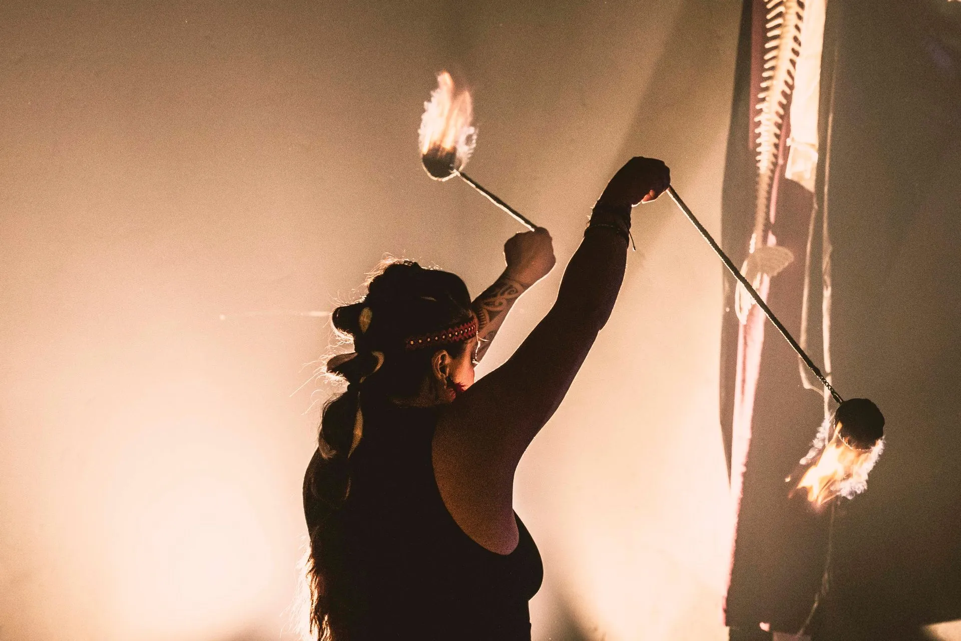 A woman in a black tank top is juggling two sticks of fire.