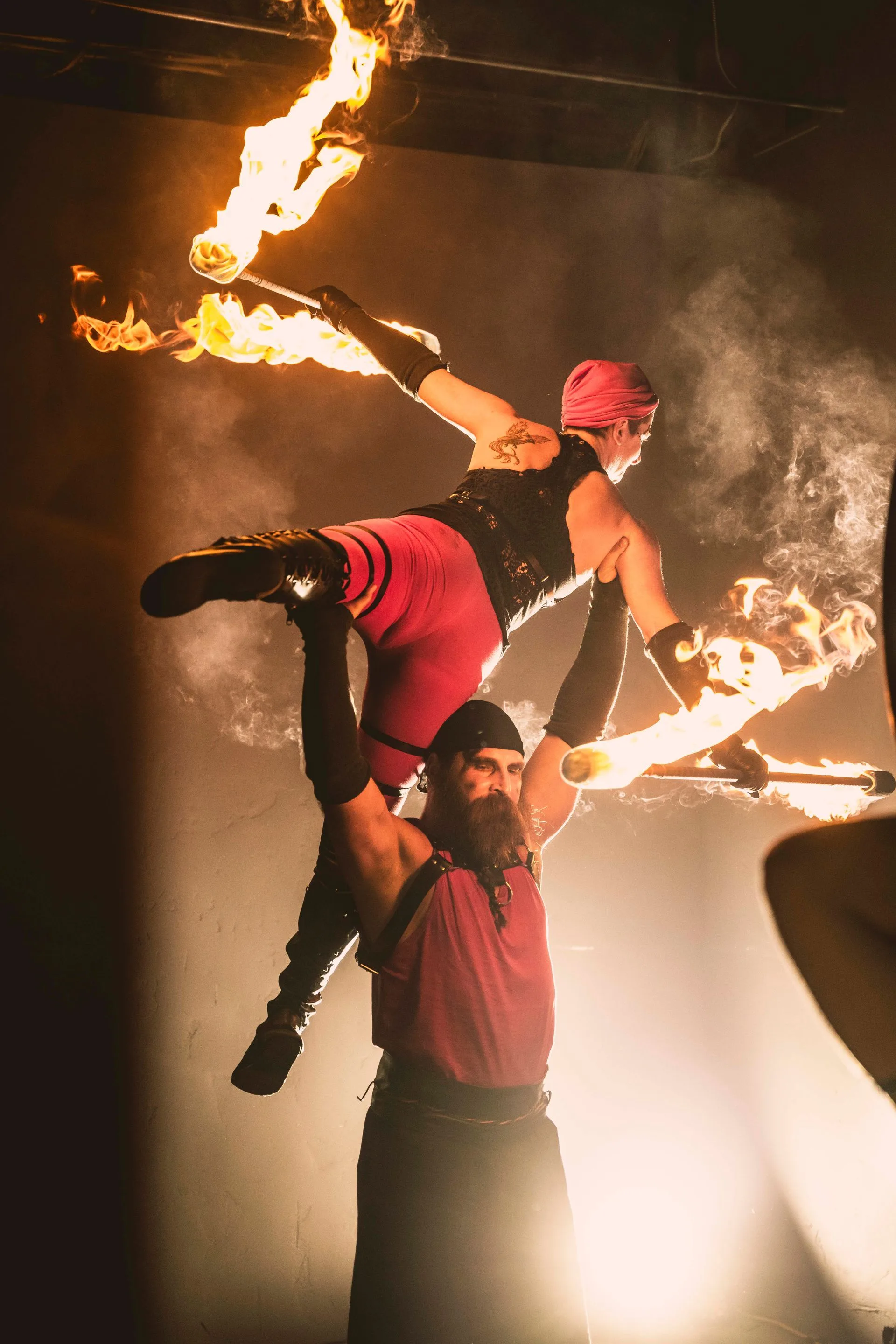 A man is carrying another man on his shoulders while they perform a fire show.