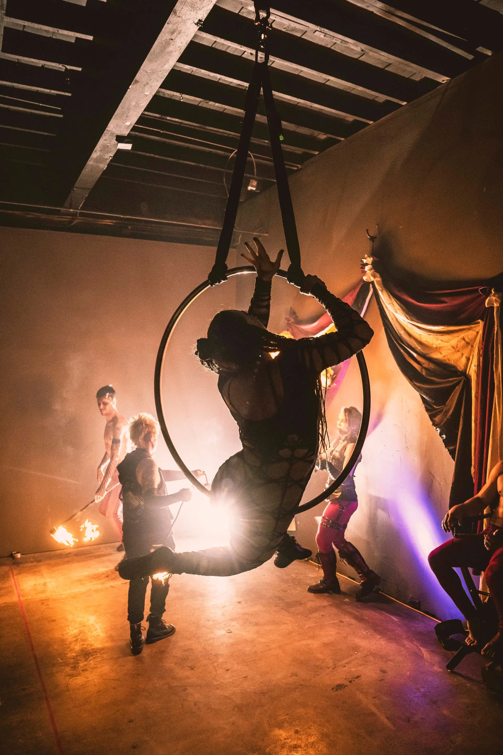 A man is hanging from an aerial hoop in a dark room.