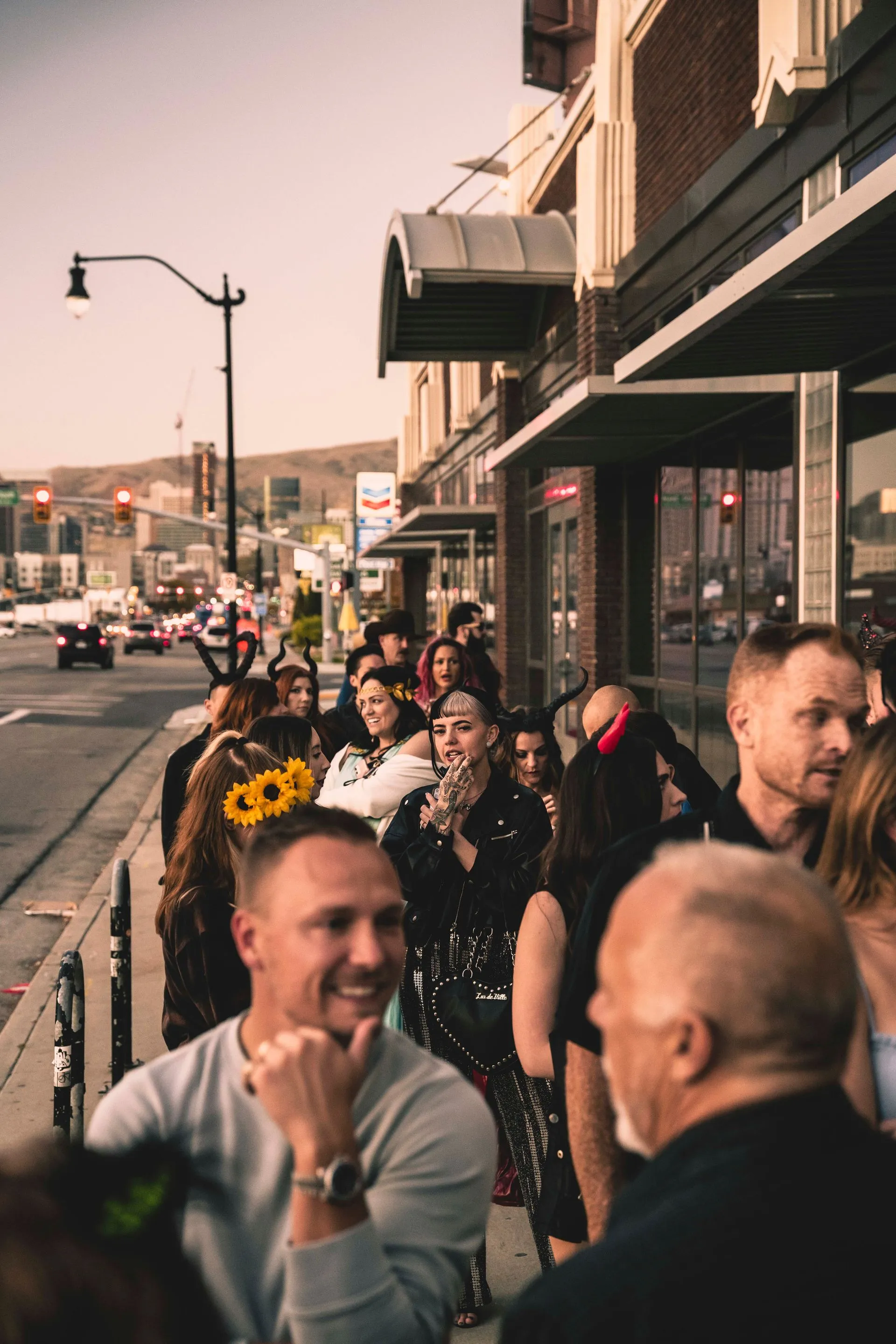 A group of people are standing on the sidewalk in front of a building.
