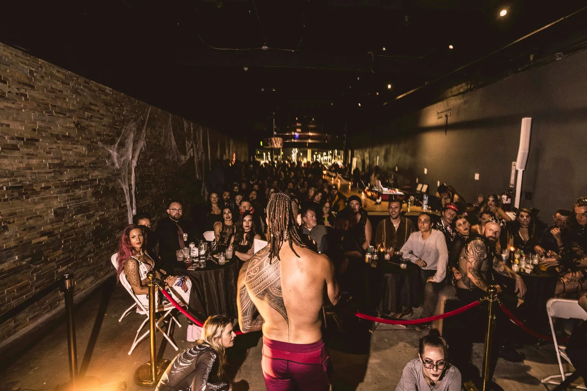 A man without a shirt is standing on a stage in front of a crowd of people.