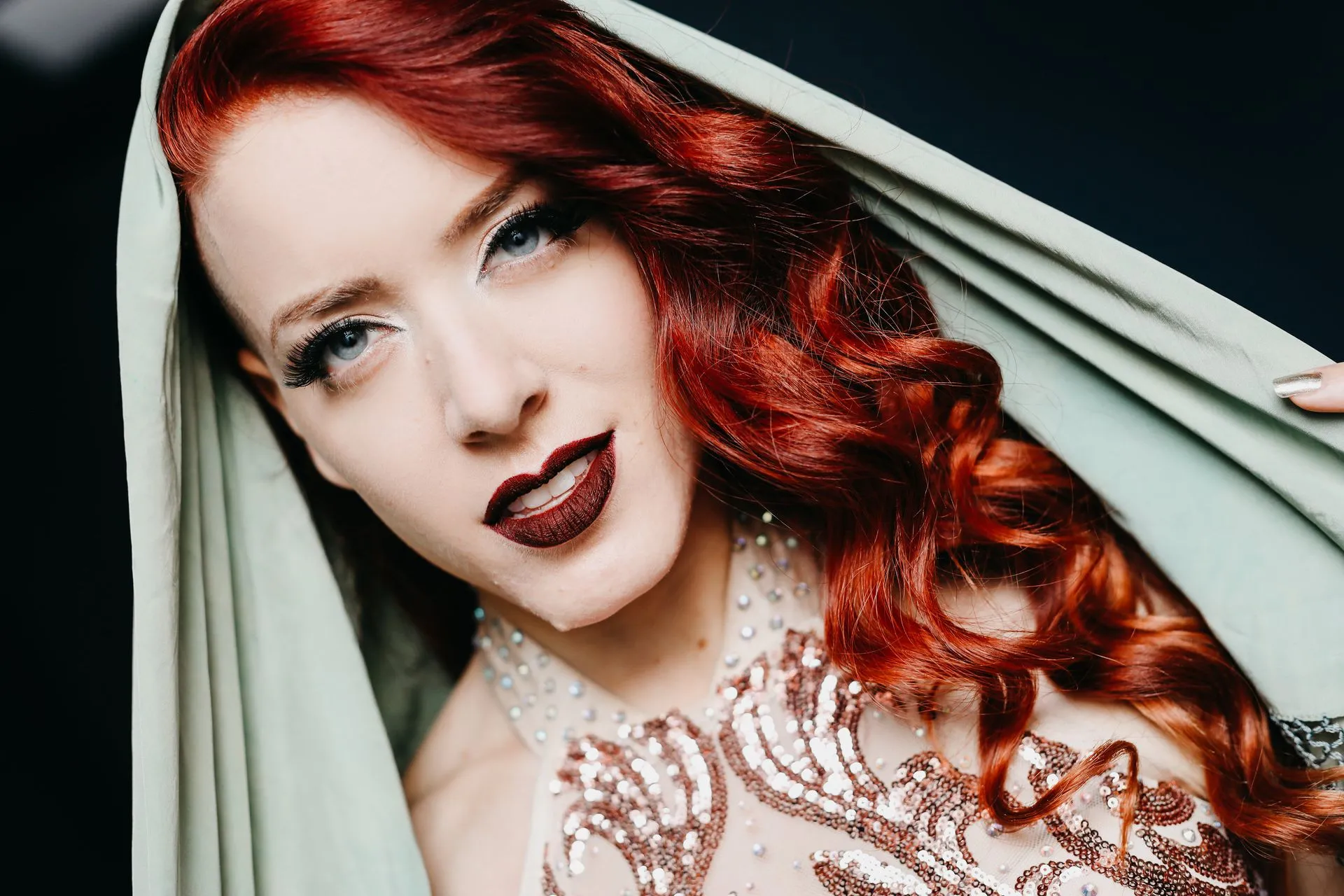 A woman with red hair is covering her face with a green cloth.