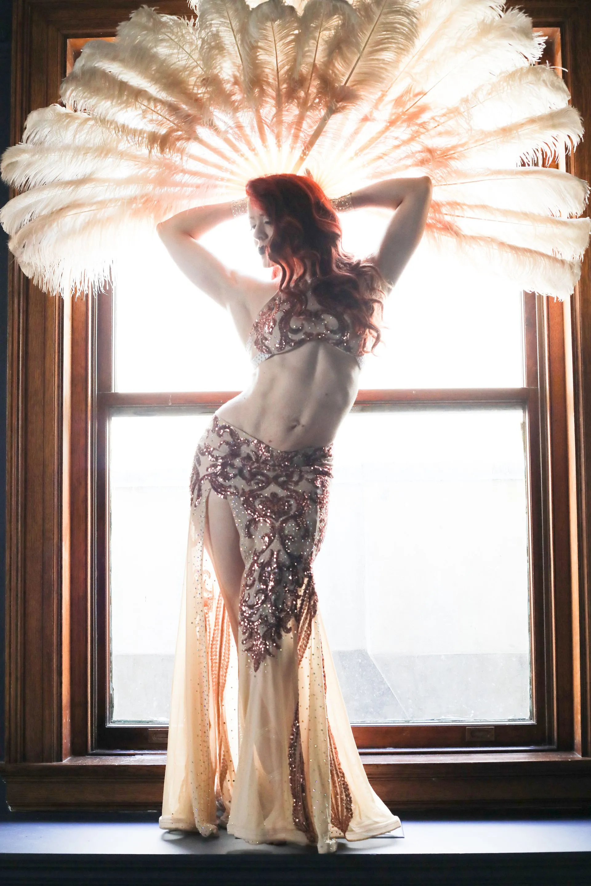 A woman is standing in front of a window holding a fan over her head.