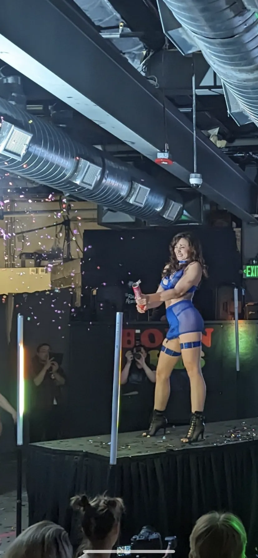 A woman is standing on a stage in a club holding a microphone.