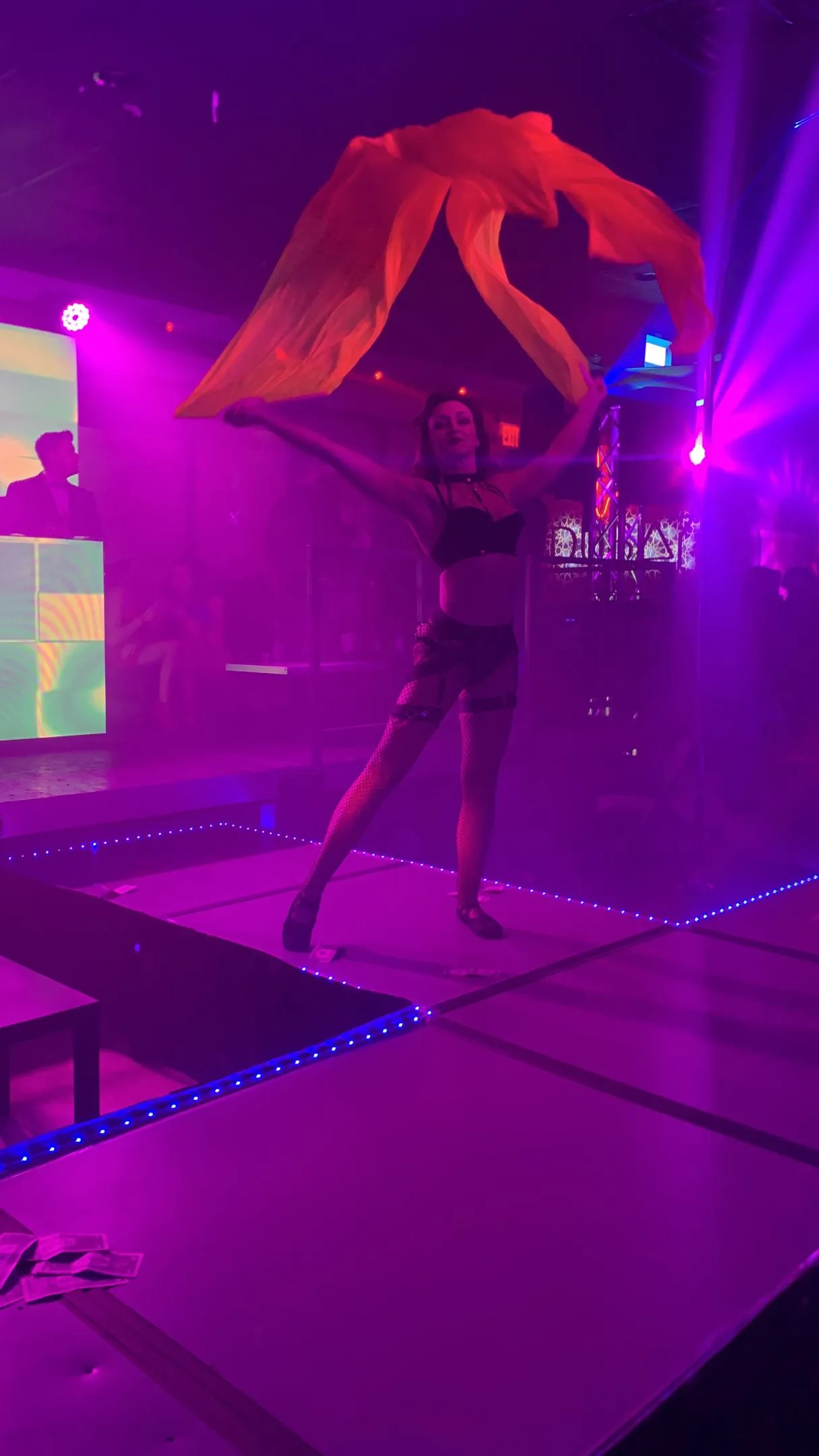 A woman is dancing on a stage in a dark room with purple lights.