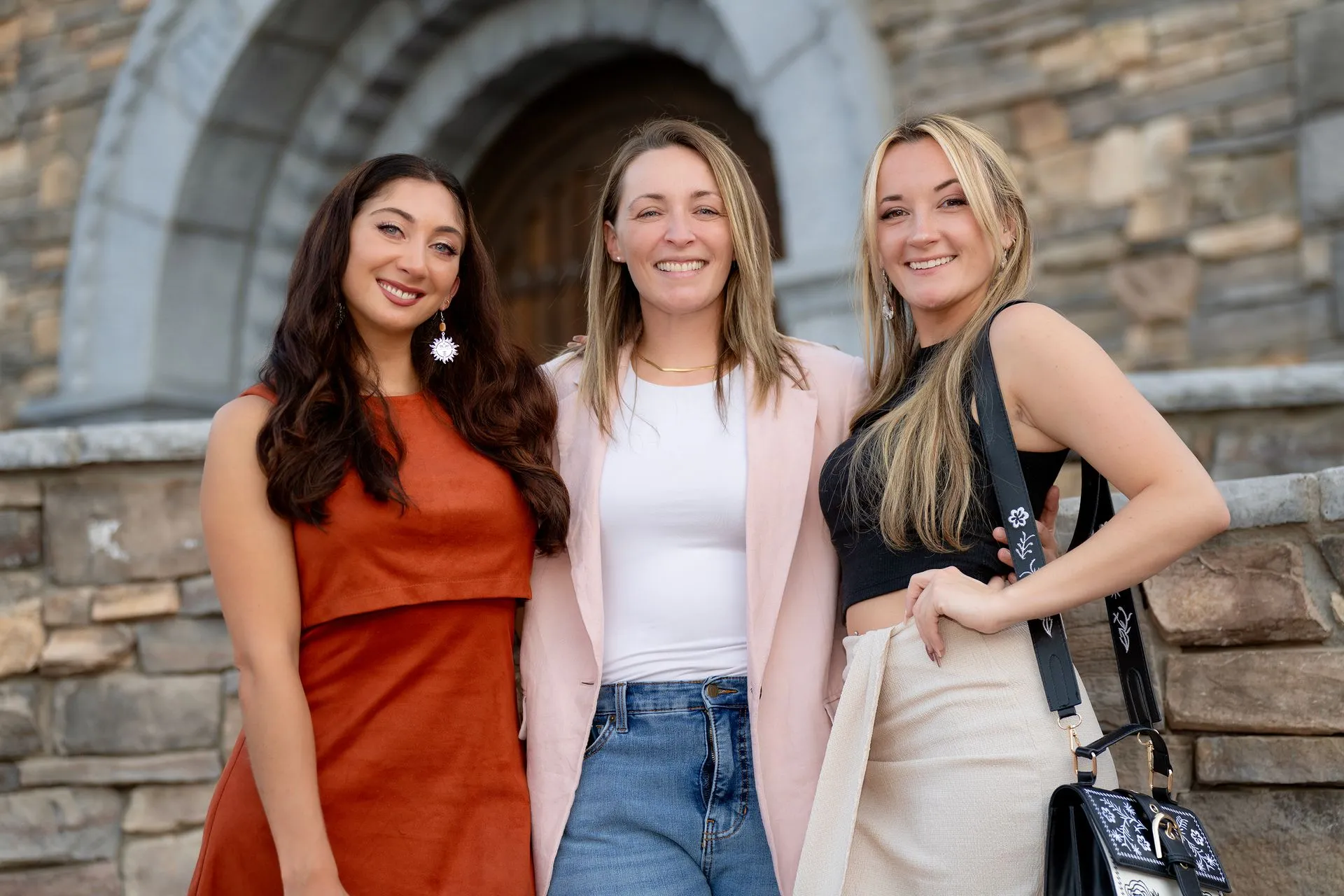 Three women are posing for a picture in front of a stone wall.