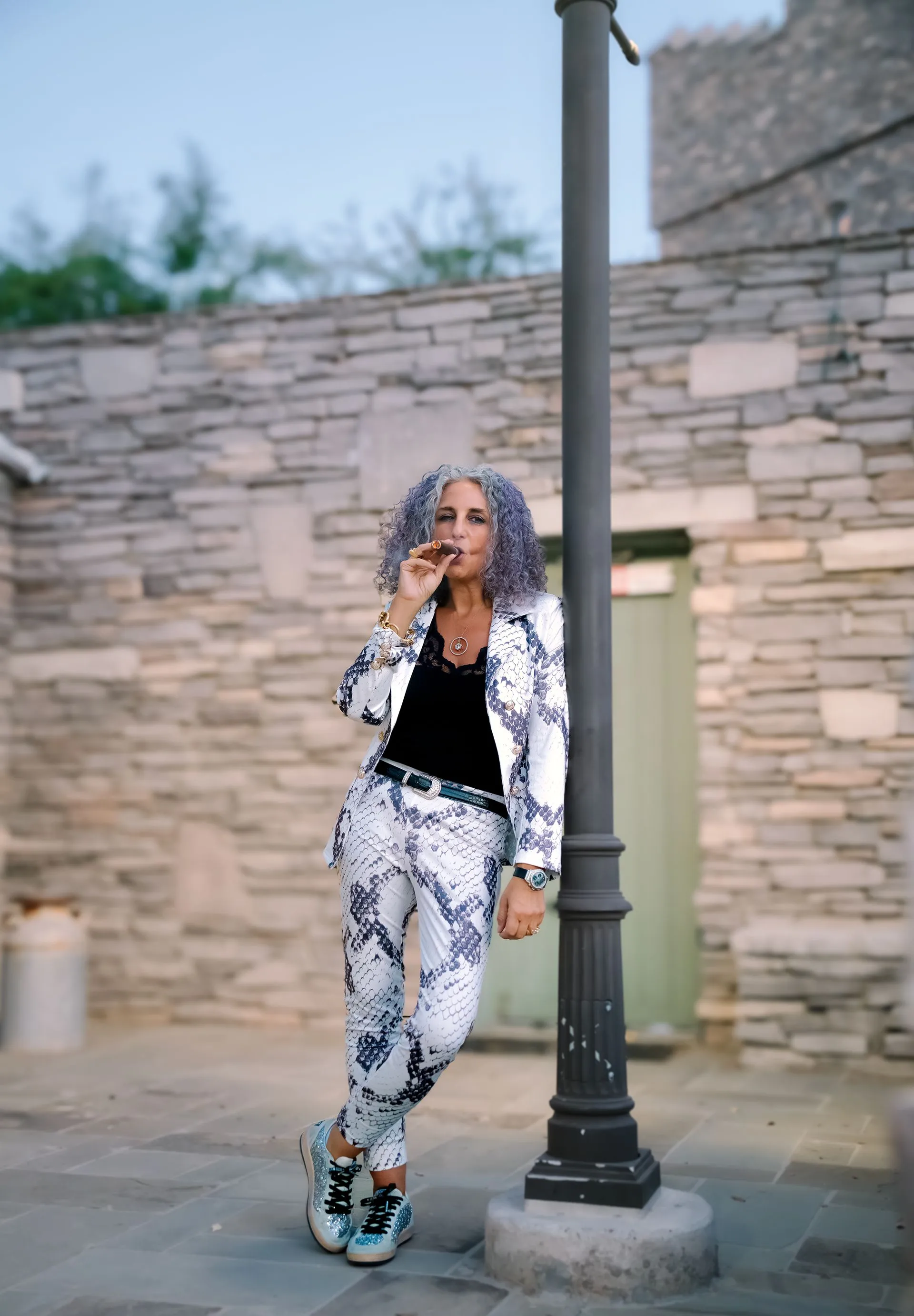 A woman with purple hair is leaning against a pole in front of a stone building.