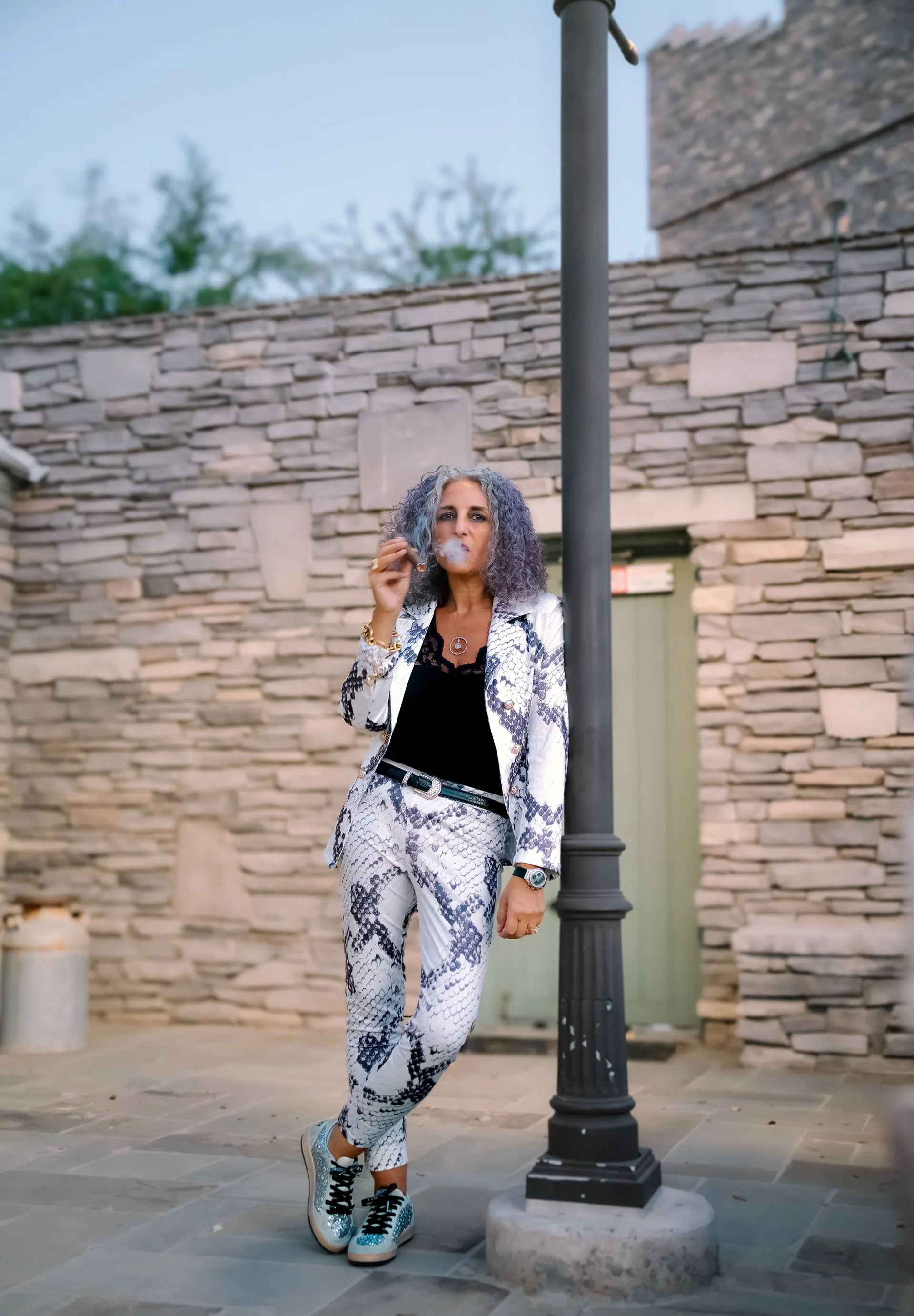 A woman with purple hair is standing next to a pole in front of a stone building.