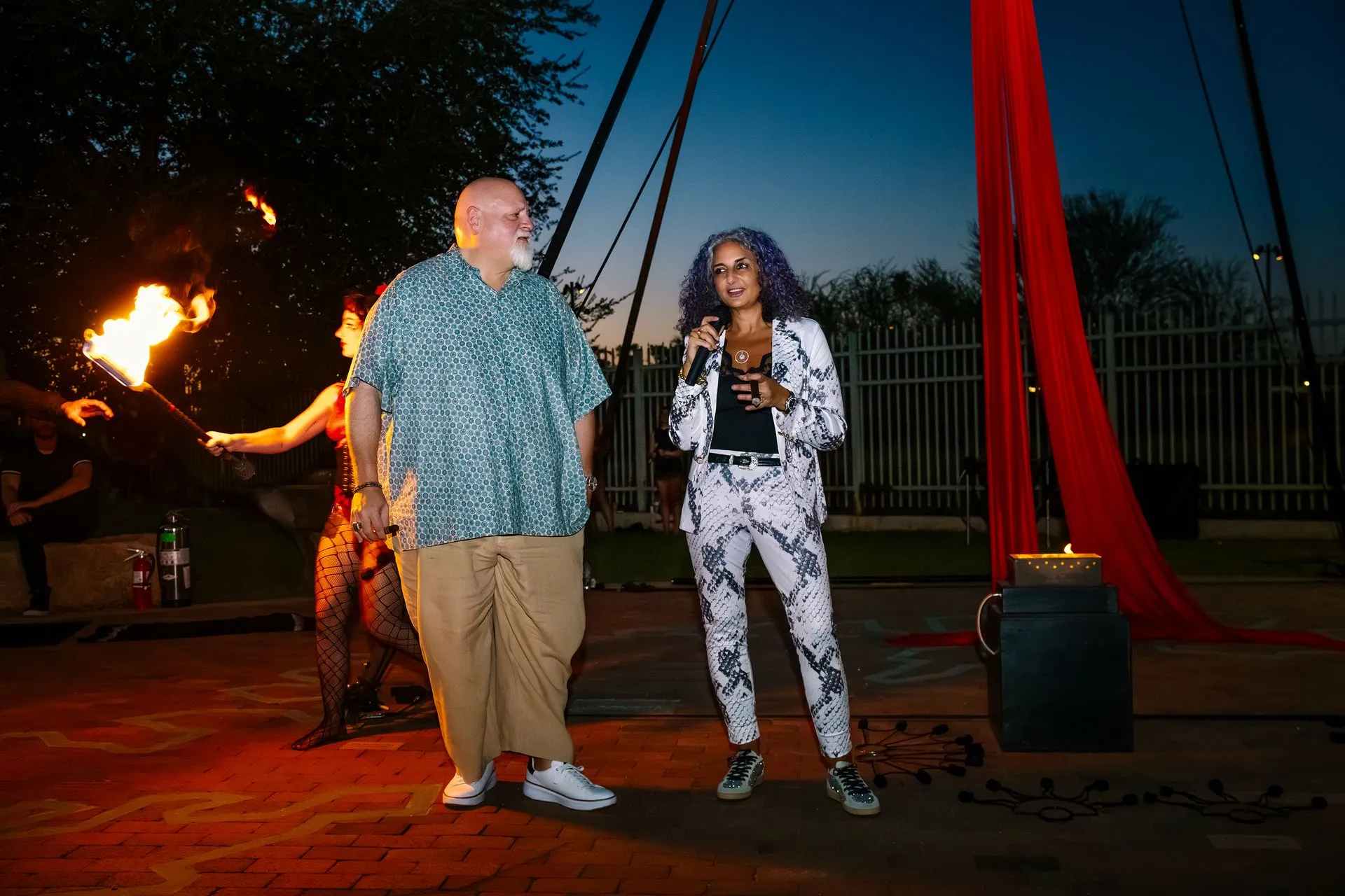 A man and a woman are standing next to each other in front of a fire performer.