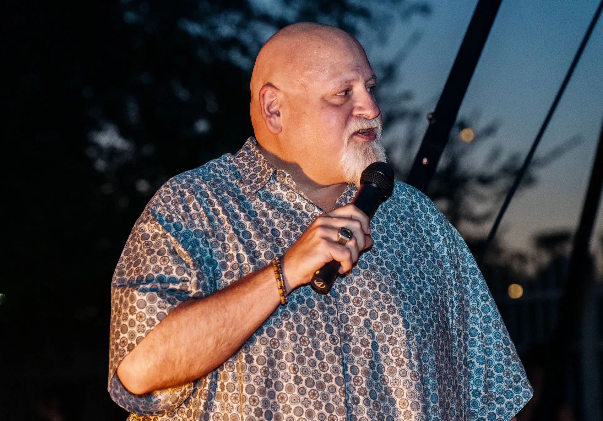 A bald man with a beard is holding a microphone in his hand.
