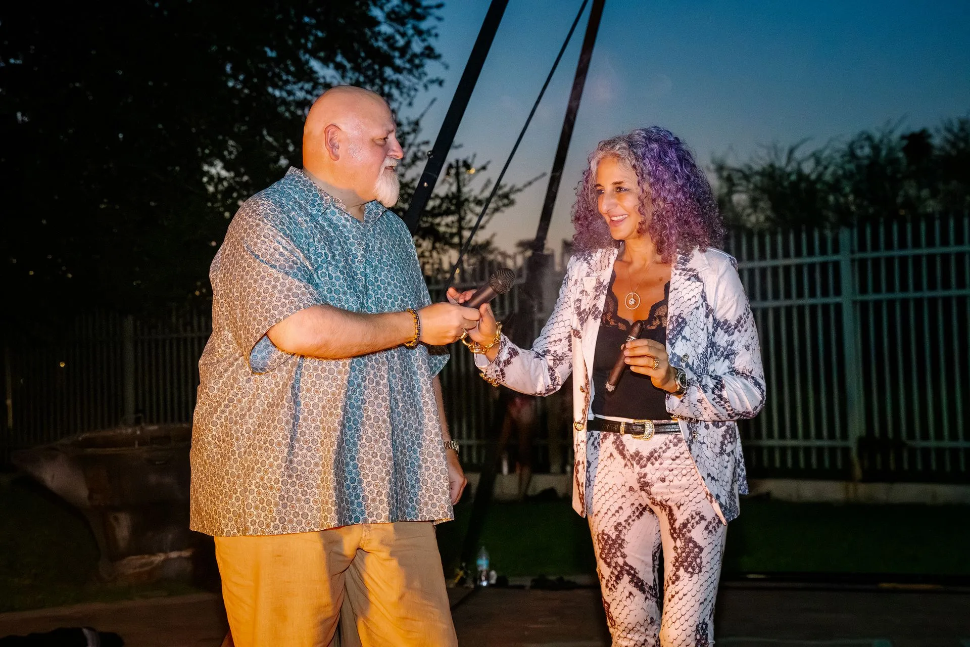 A man and a woman are shaking hands in front of a fence.