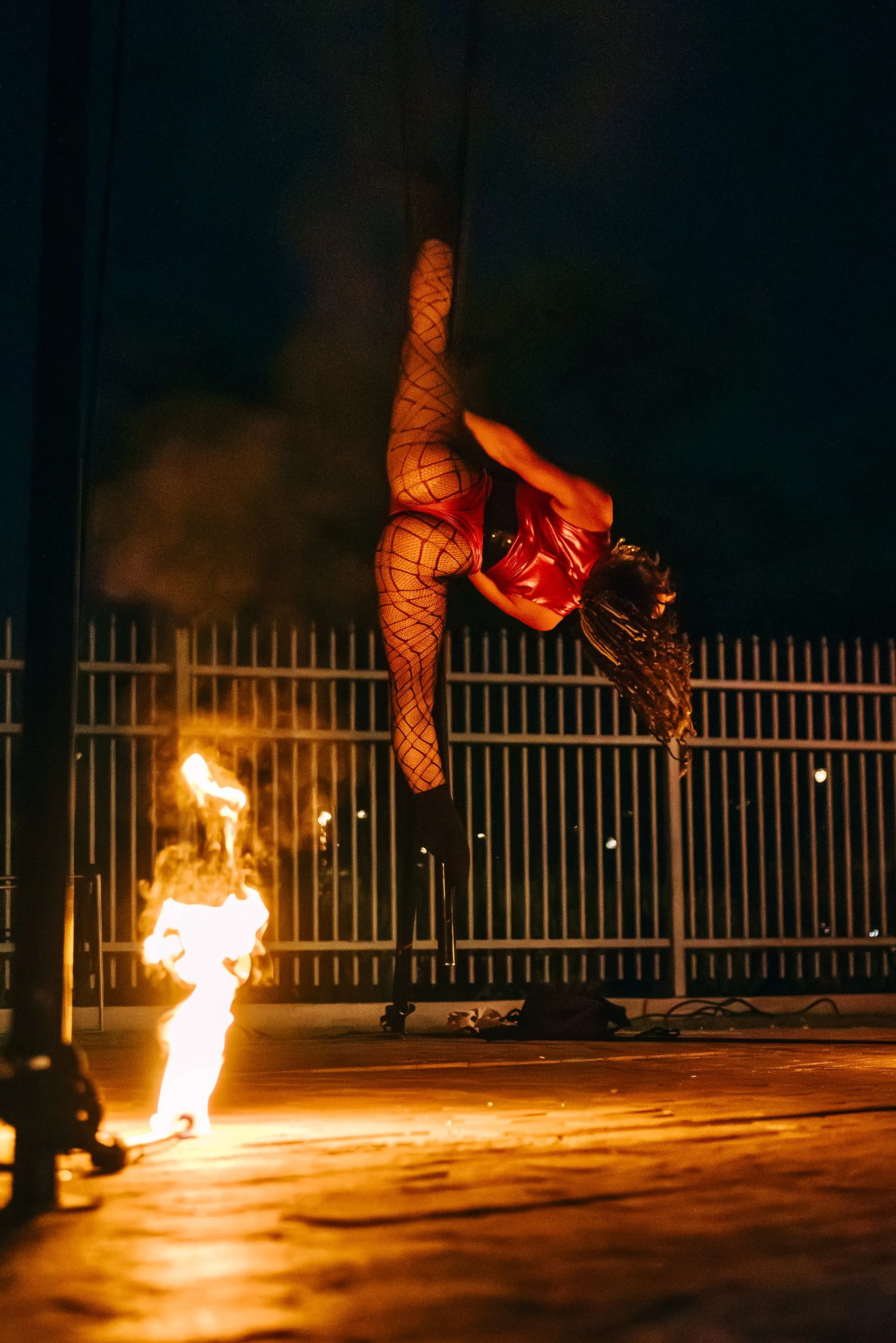 A woman is doing a split on a pole with flames coming out of it.